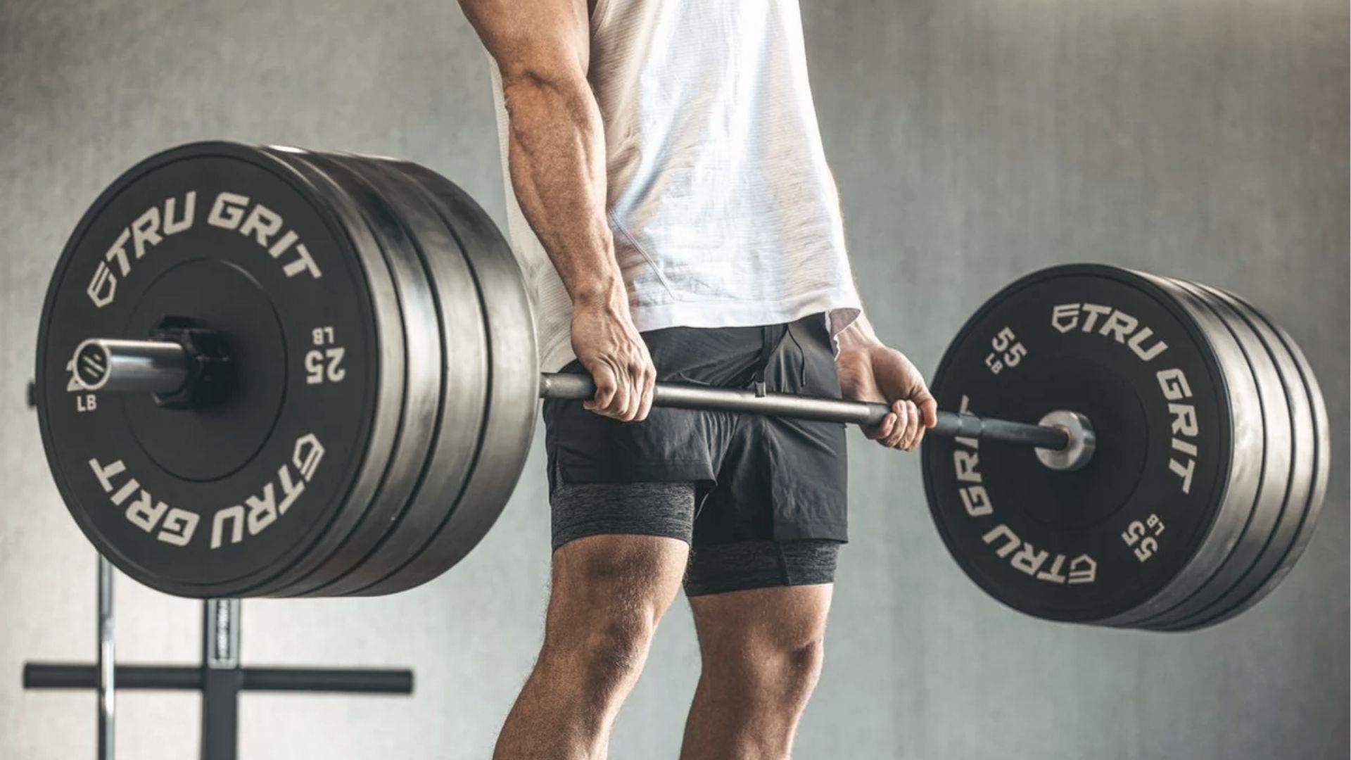 Athlete deadlifting loaded Olympic barbell with TRU GRIT plates in a modern gym setting.