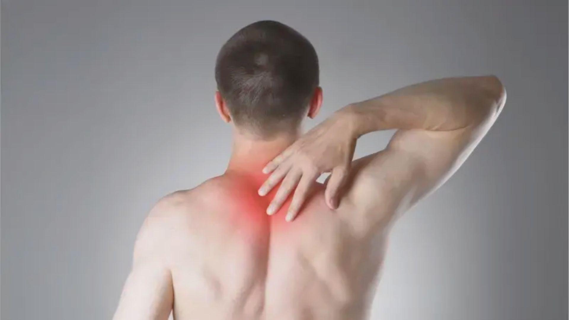 Shirtless man viewed from behind grips upper back and neck with red highlight on the area.
