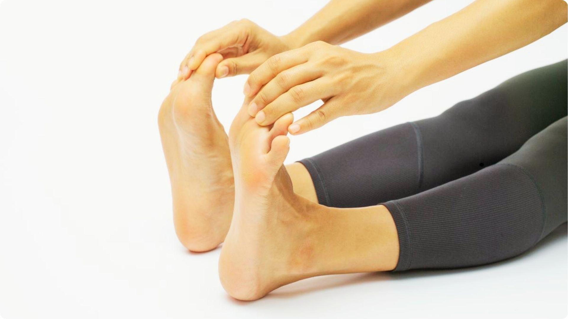A person sitting on a white background gently pulls back on their big toes with both hands to stretch the feet.