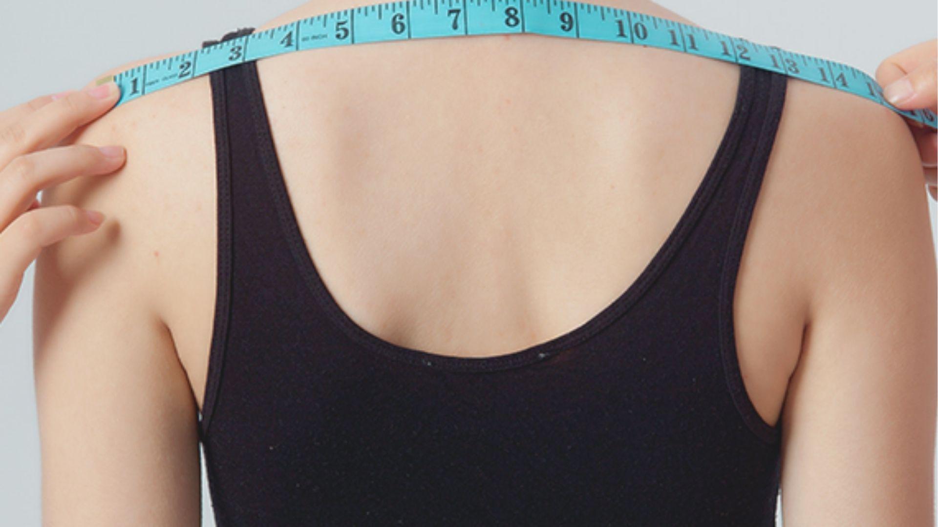 Close-up of a woman’s back in a black tank top with a blue measuring tape stretched across her shoulders.