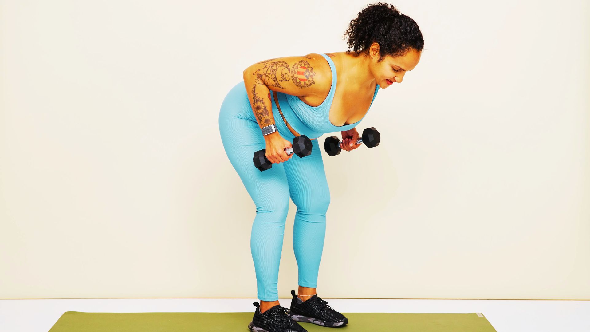 Woman in blue workout set performs dumbbell bent-over rows against a white background.