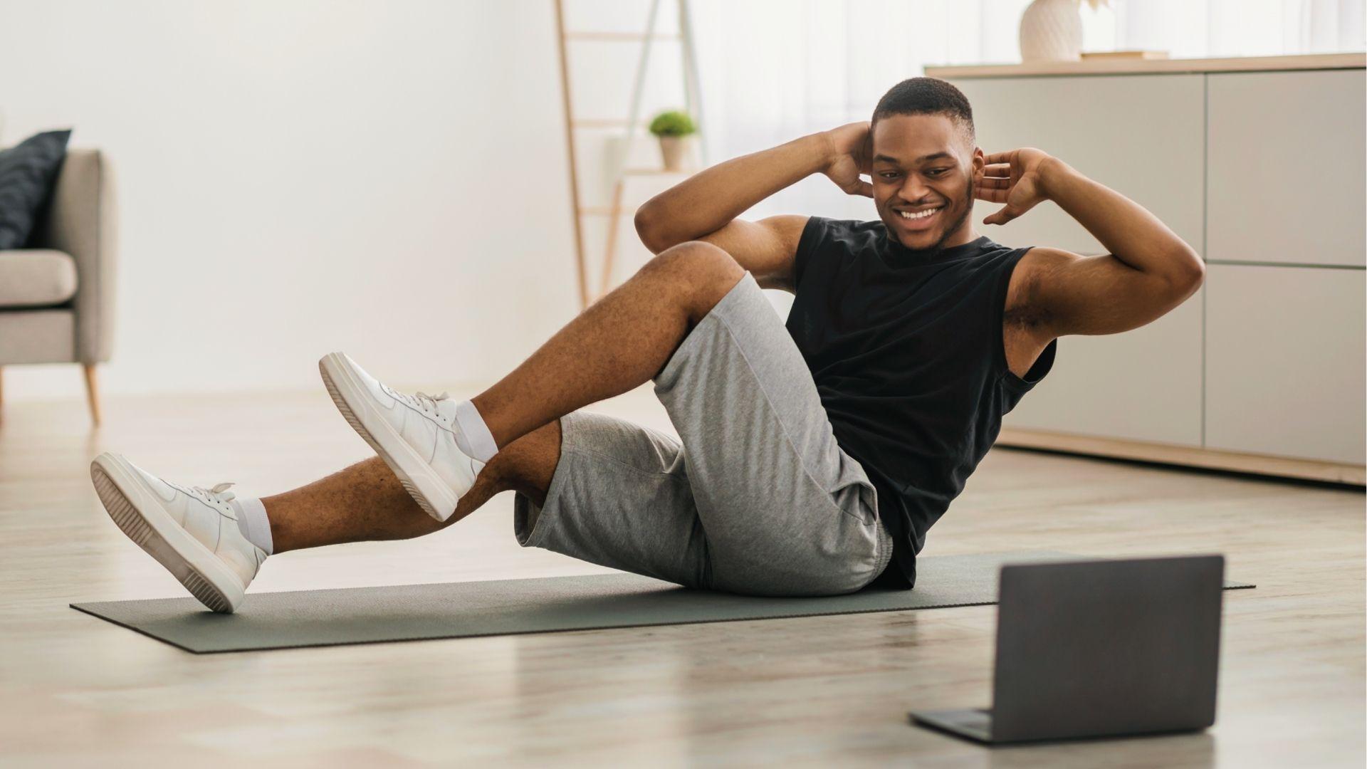 Man does bicycle crunches at home following laptop guide for 28 day calisthenics core day.