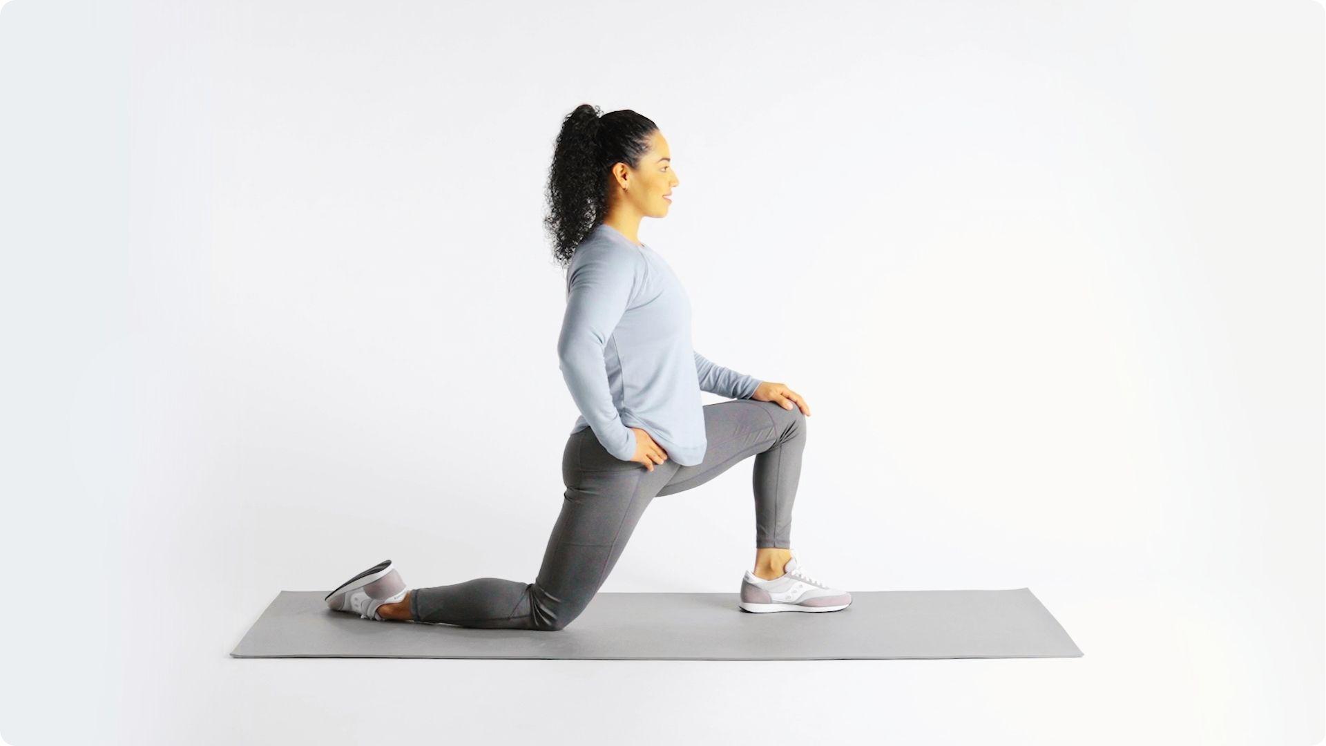 Woman in gray activewear performing a kneeling hip flexor stretch on a mat with front knee bent at 90 degrees.