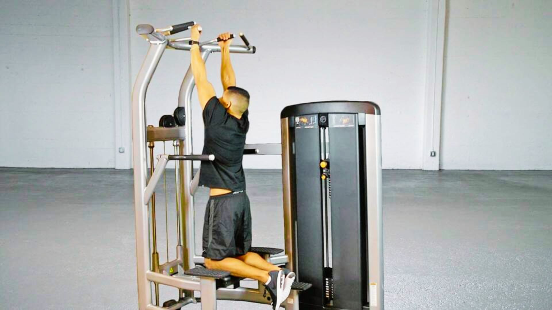 Man hanging from pull-up bar in gym with engaged shoulders and straight posture.