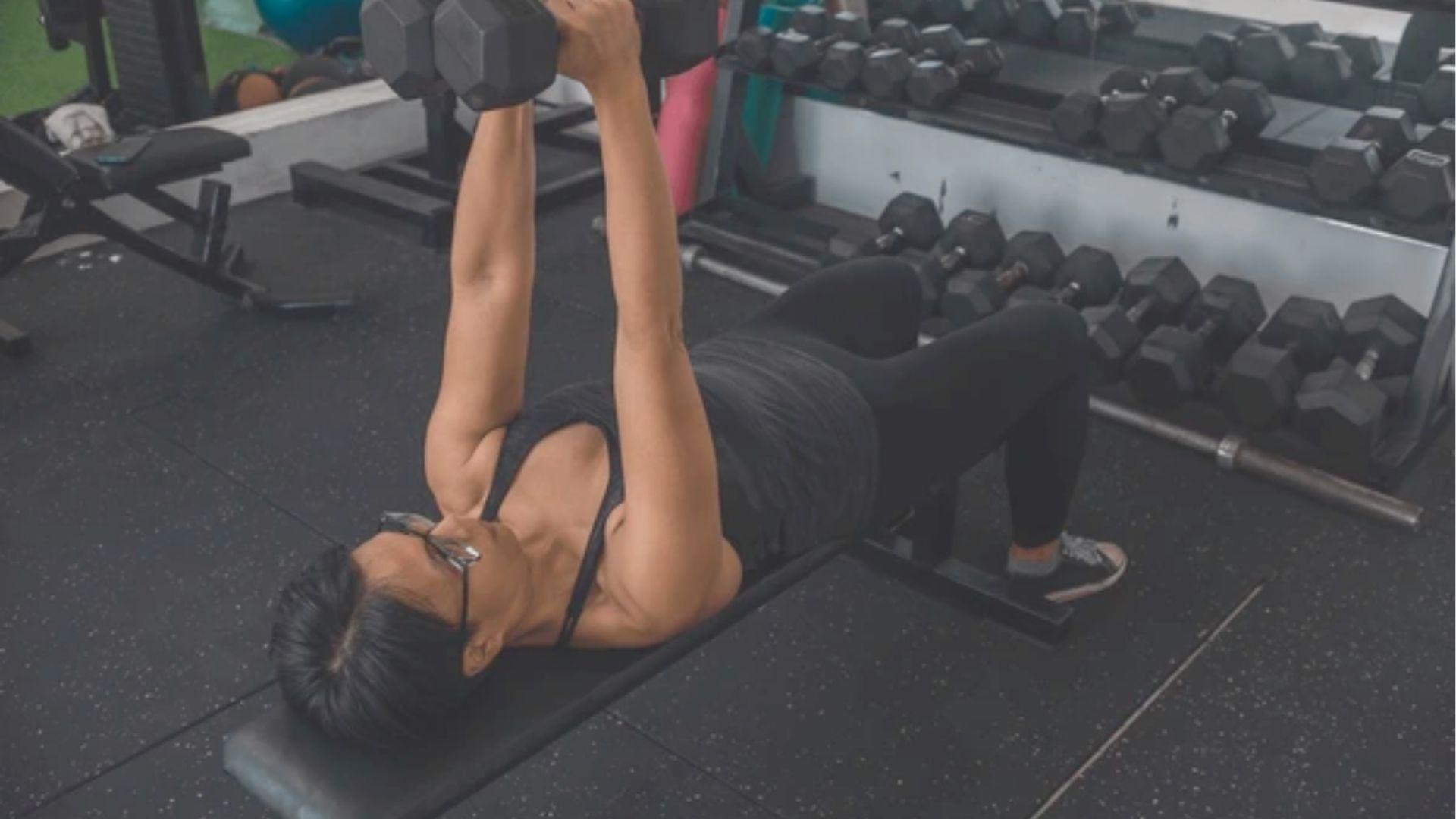 Woman lying on a flat bench performing a close-grip dumbbell press in a gym.