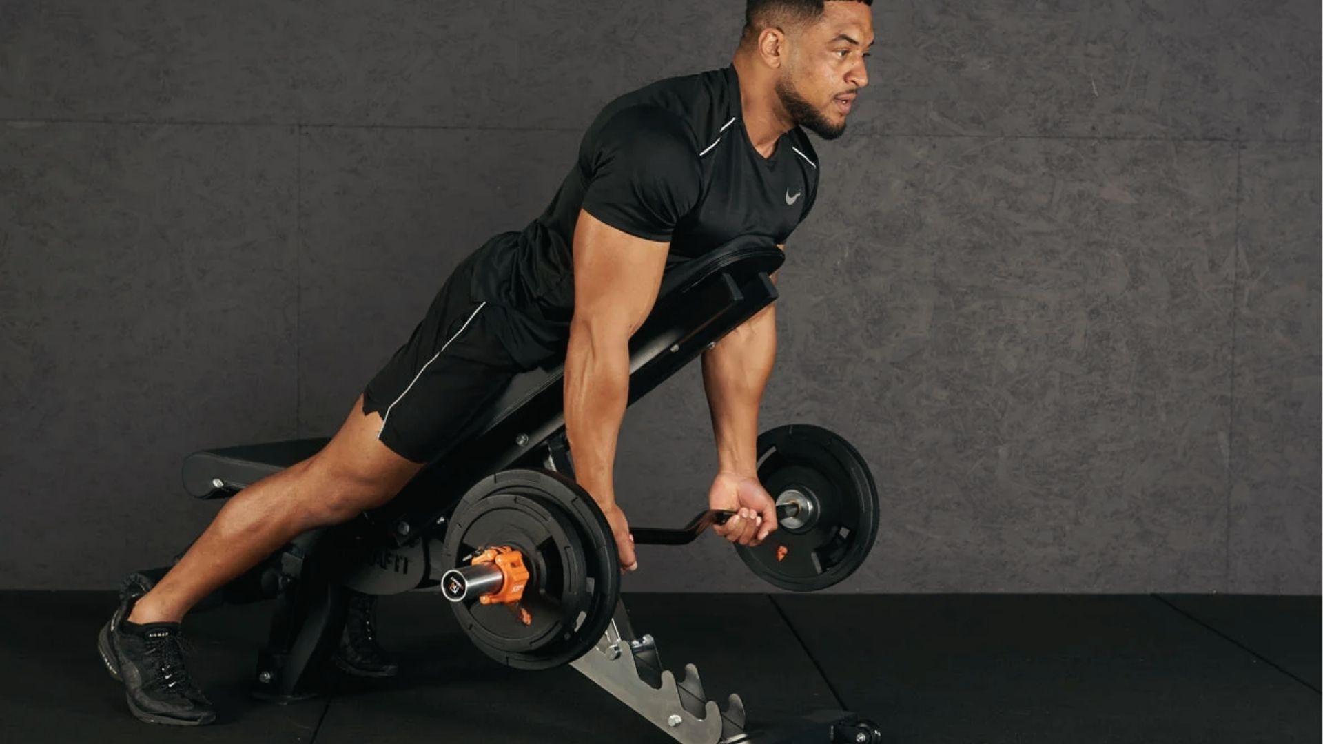 Athlete in black Nike shirt does barbell spider curls on an incline bench, arms extended, focused on form.