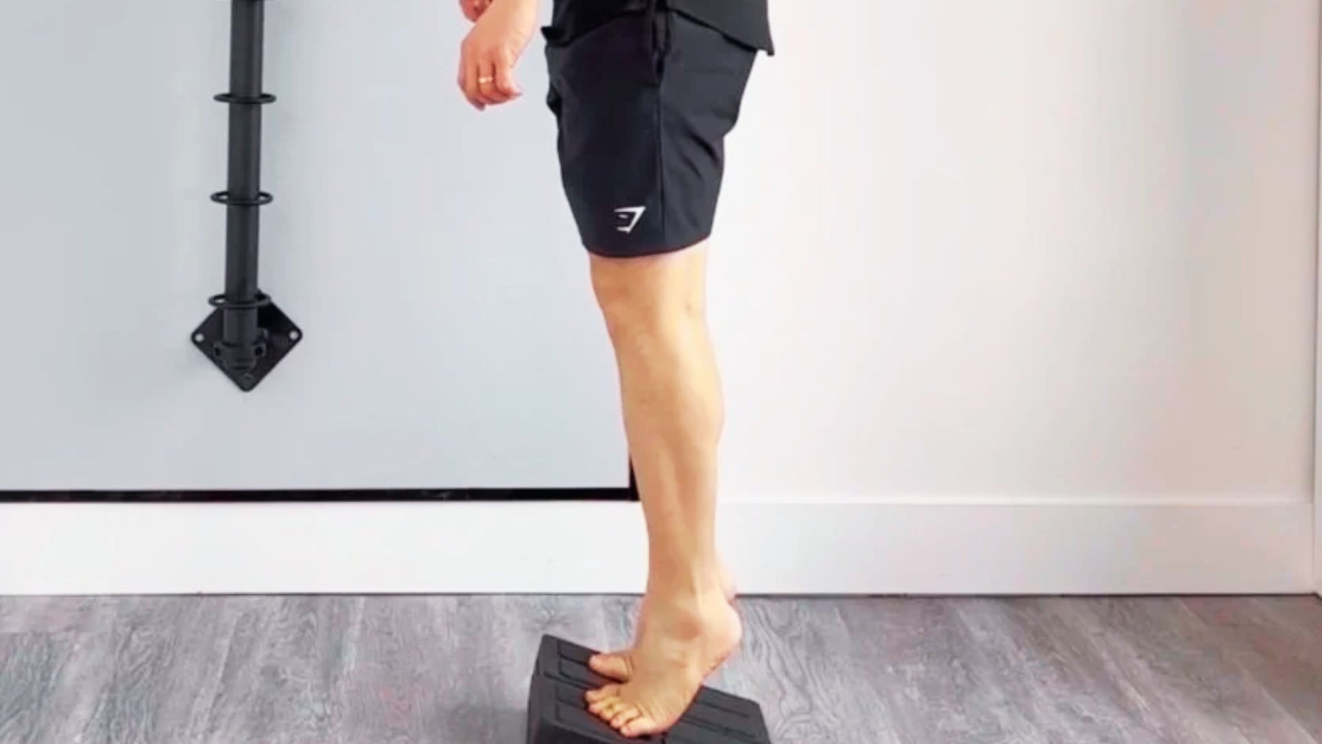 A person stands barefoot on a black slant board doing calf raises.