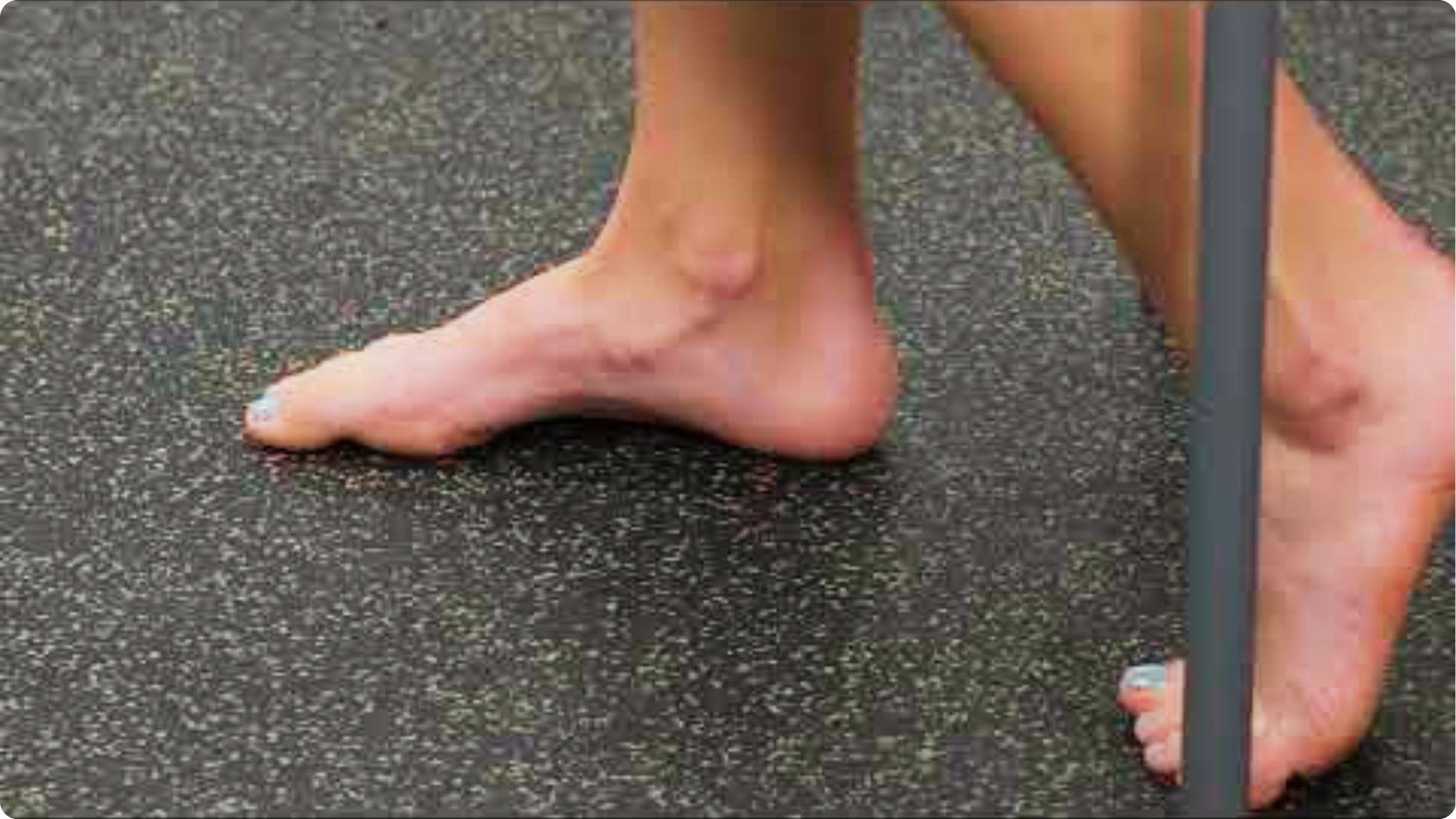 Bare feet on gym flooring with one foot lifting the arch while keeping toes and heel on the ground.
