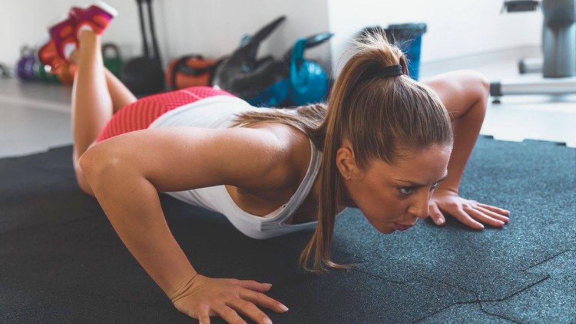 Woman doing push-ups with knees on mat in a gym, showing lumbar extension.