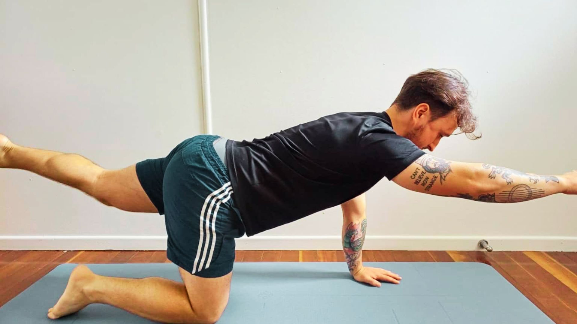 Man on yoga mat in quadruped position extending opposite arm and leg for stability.