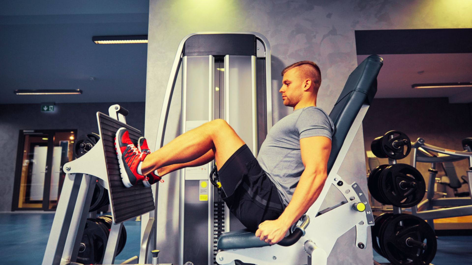 Man in grey shirt and red shoes uses the seated leg press machine with focused form.
