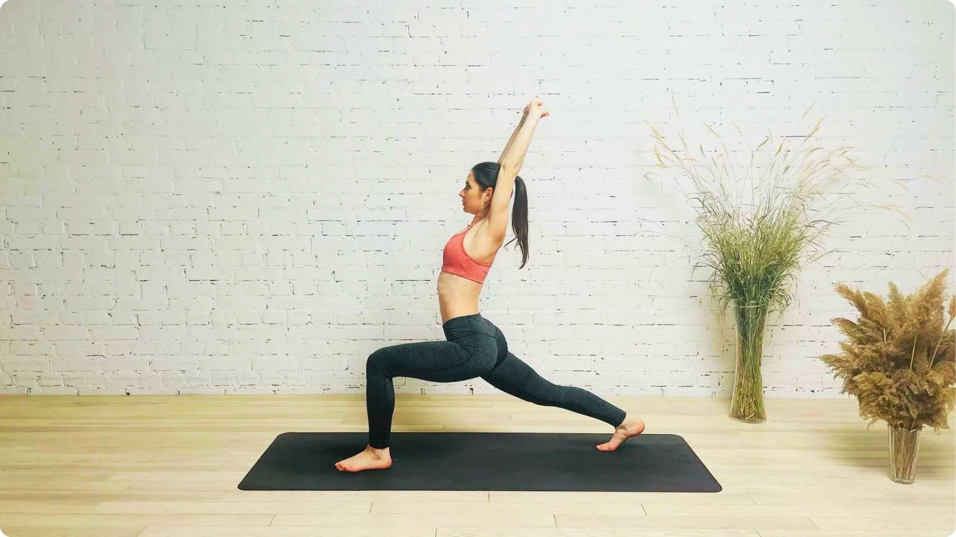 Woman in coral sports bra doing a low lunge on a yoga mat with arms raised overhead.