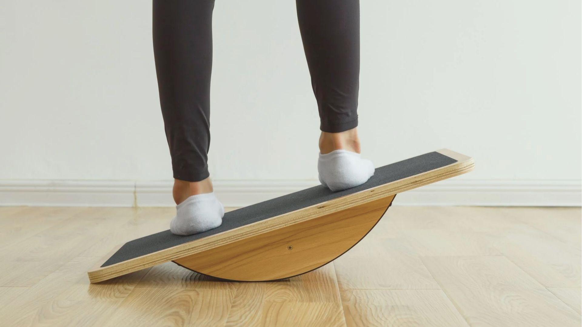 Close-up of feet in white socks rocking side-to-side on a wooden wobble board with black grip.