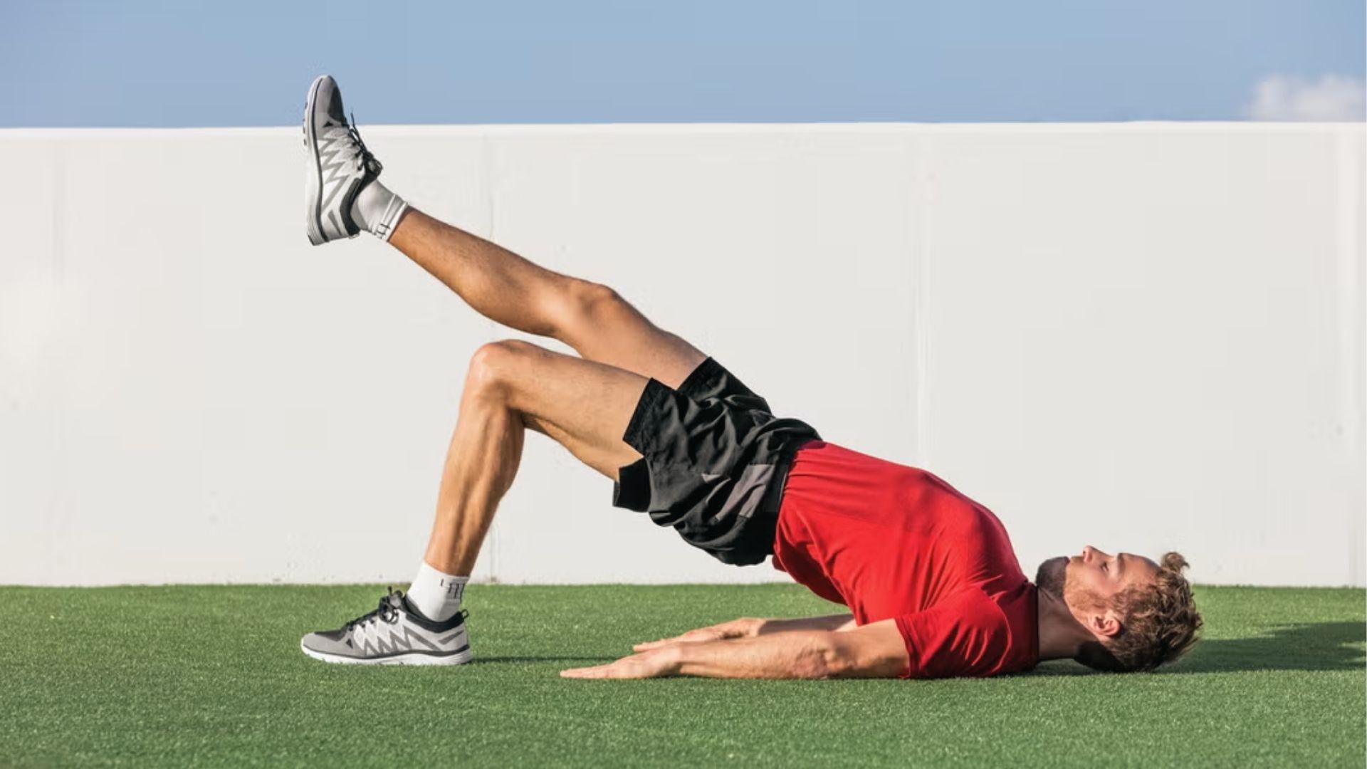 Man doing single-leg glute bridge on grass to activate glutes, the key hip extension muscles