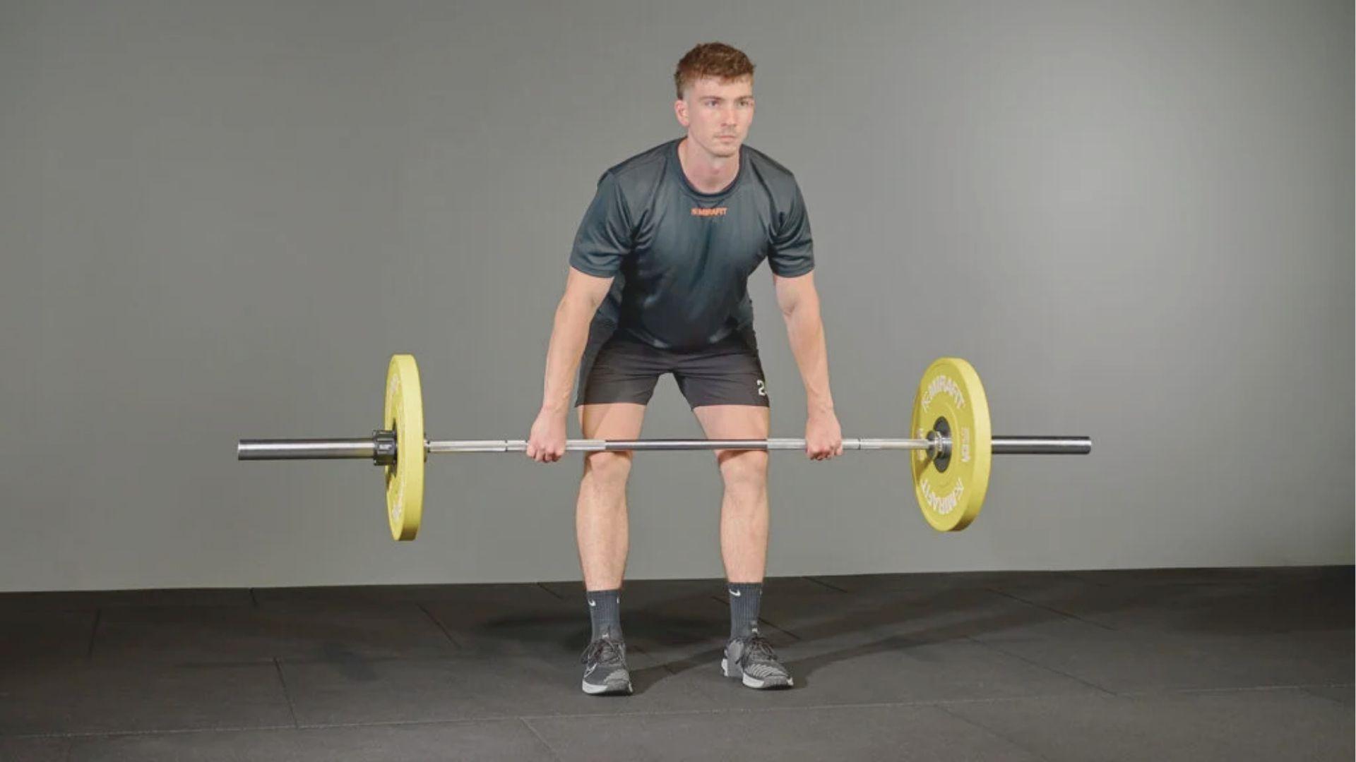 Male athlete in hang position holding barbell just above knees, preparing to explosively extend upward.