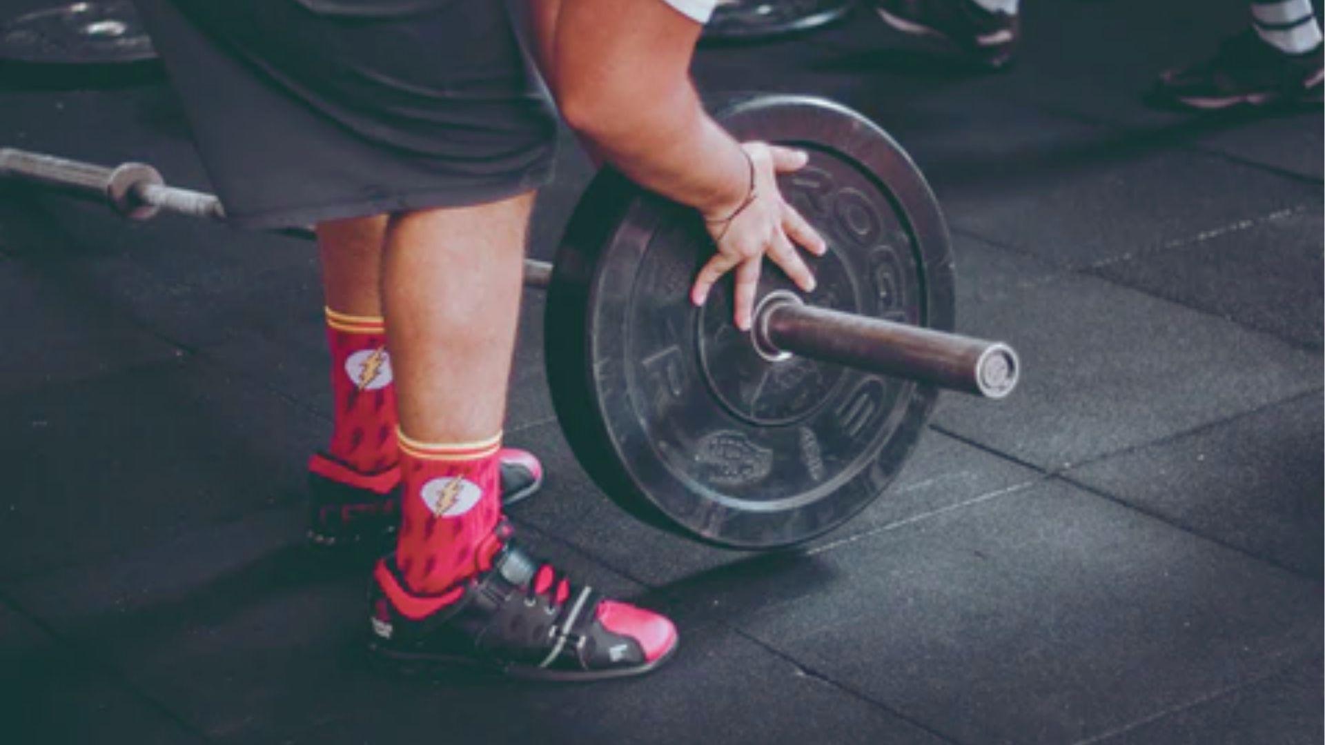 Close-up of a person’s hand adjusting a barbell plate while wearing red Flash socks and lifting shoes.