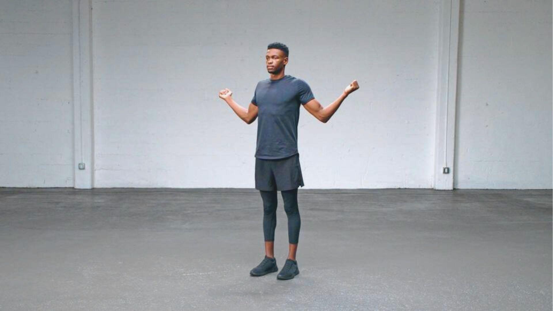 Man in dark workout clothes stands with elbows bent at 90 degrees in a goalpost position.