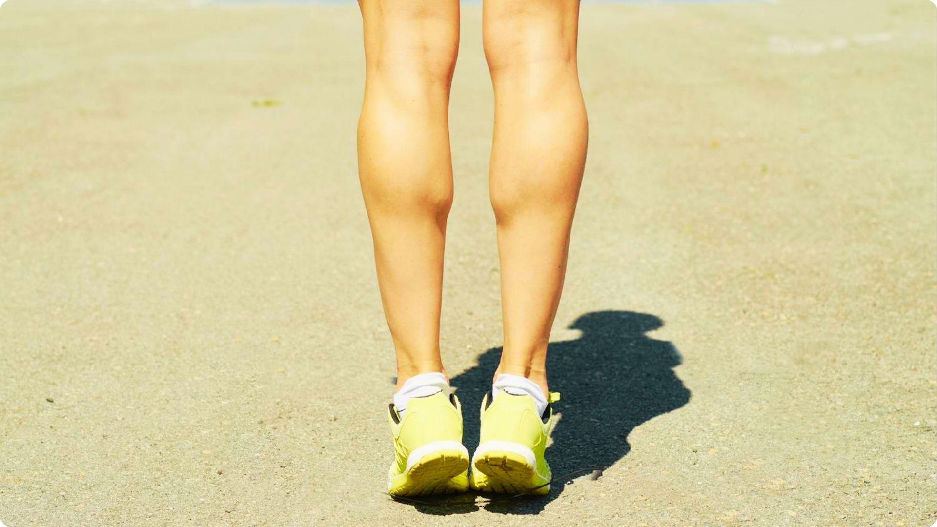Rear view of a person in yellow sneakers doing calf raises outdoors on pavement.