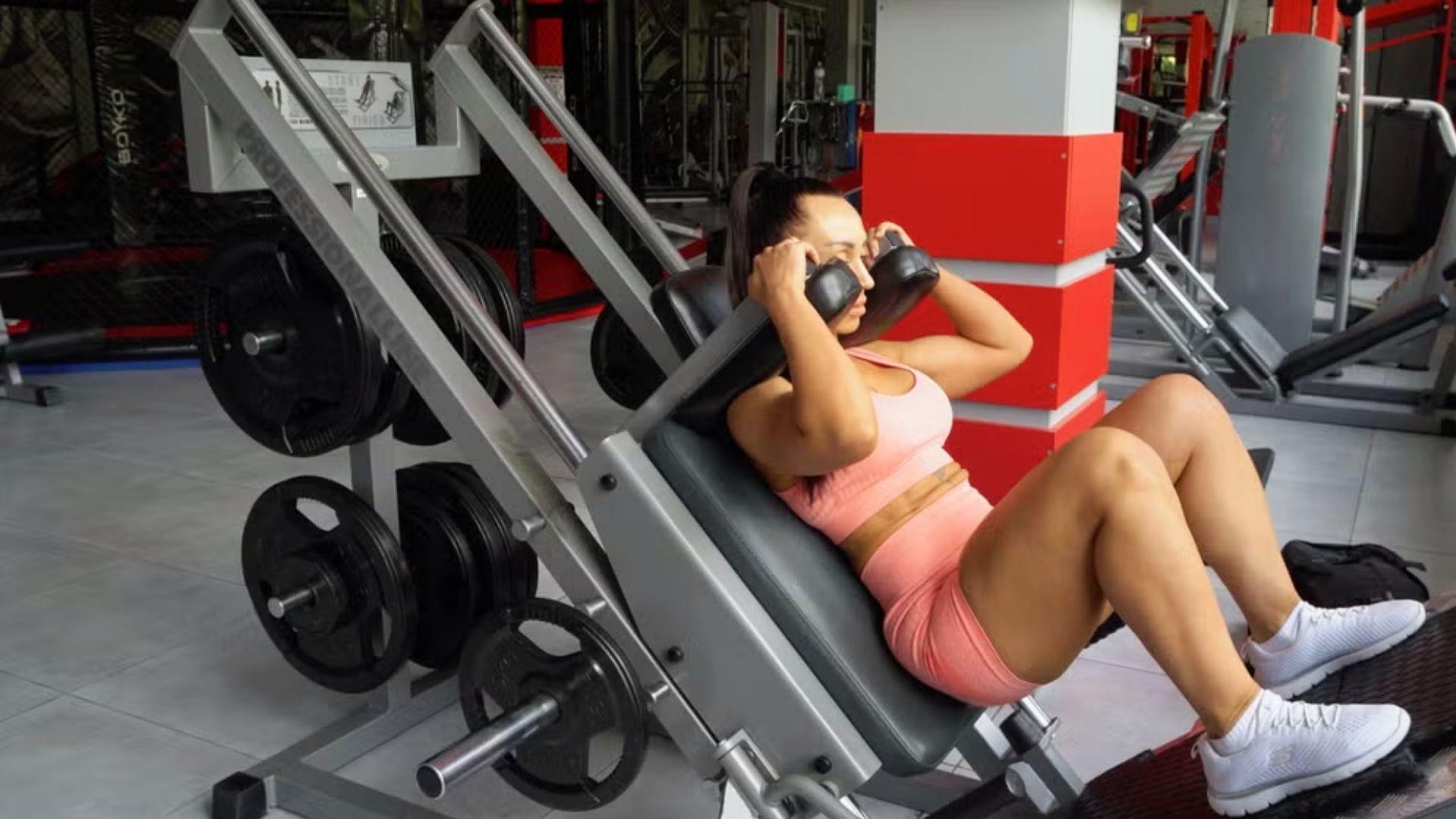 A gym user performing a hack squat on a loaded machine, highlighting lower body strength and controlled knee bend during the movement.