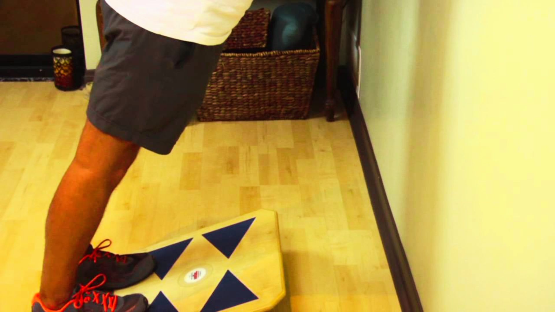 A person performs a standing calf stretch with both feet on a wooden slant board at home.