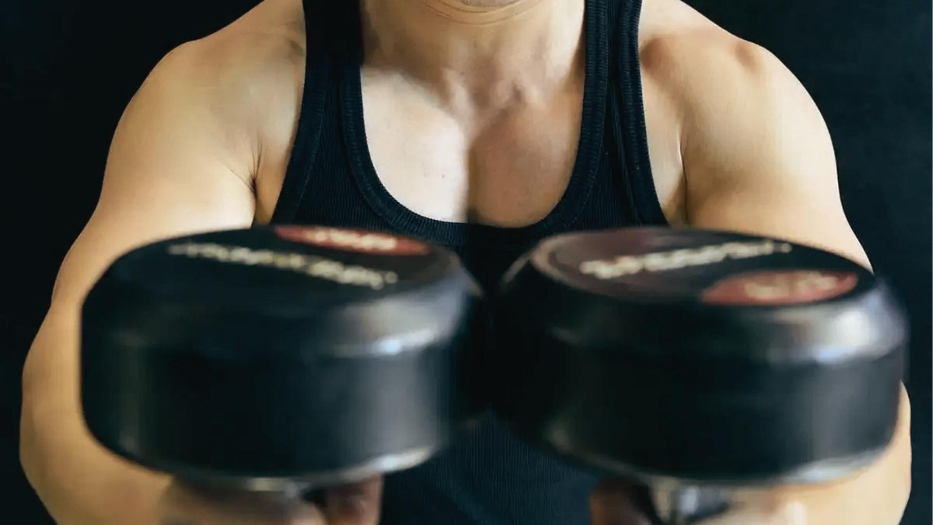 Close-up of man in black tank top holding two heavy dumbbells together at chest level for close grip press.