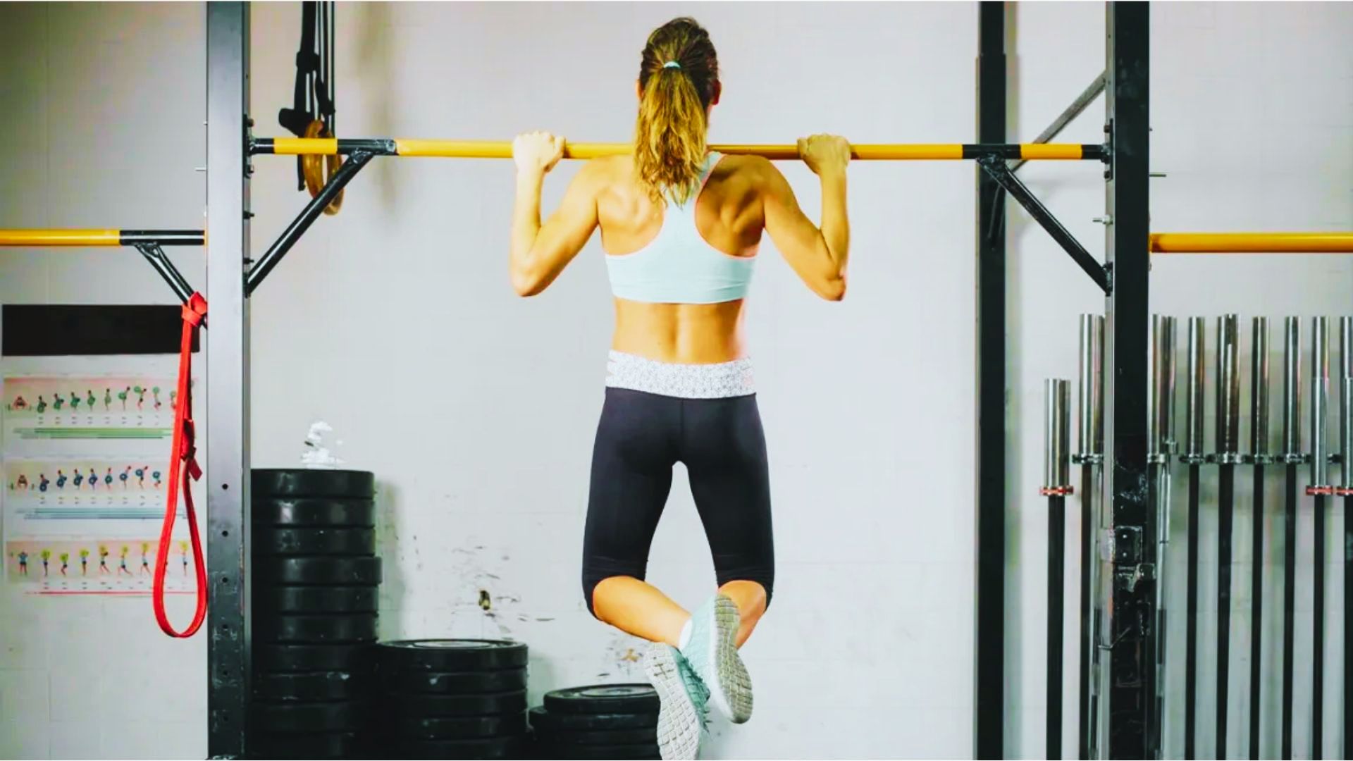 Woman performing a pull-up on a gym rig, back muscles engaged at top position.