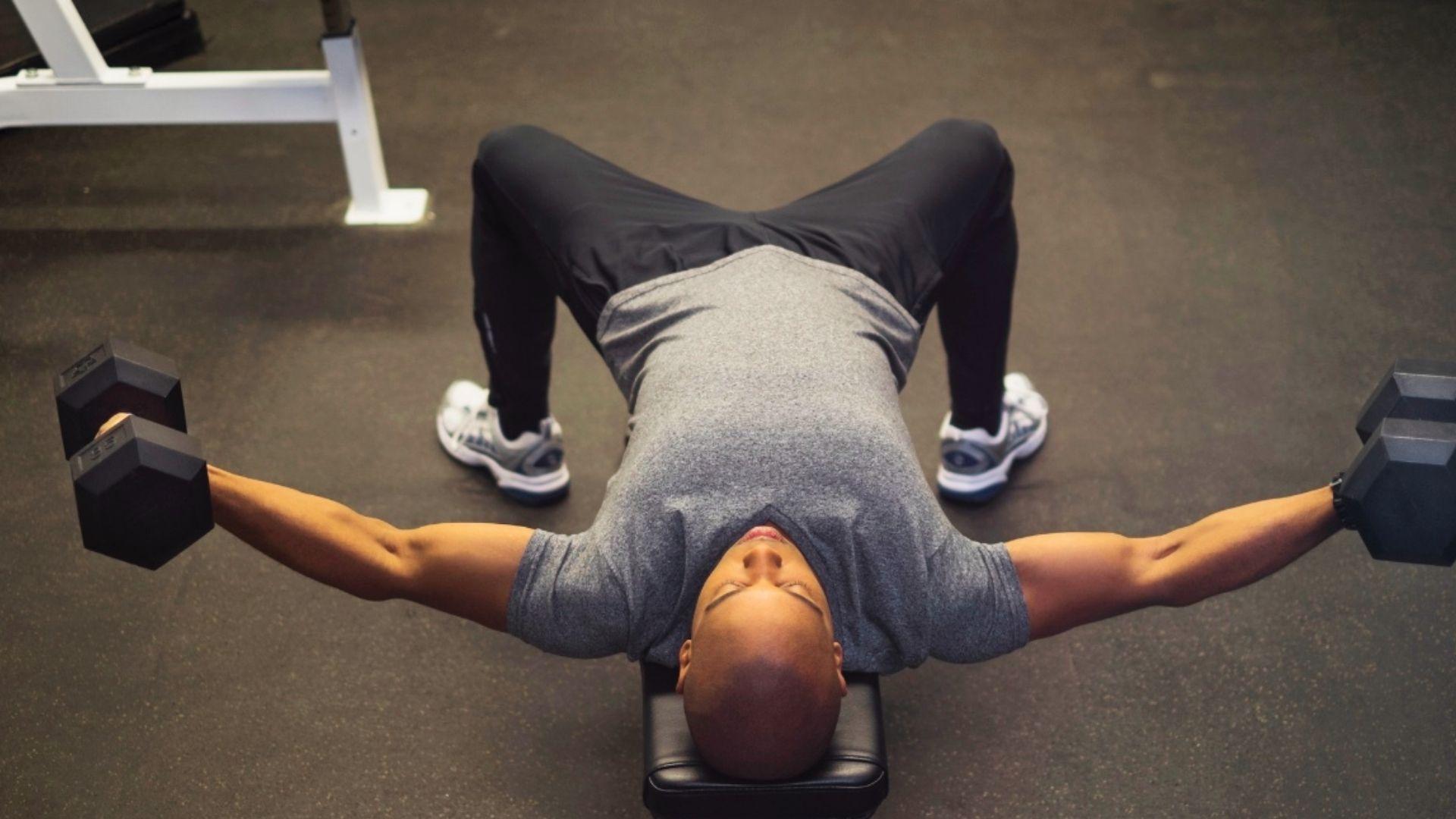 Person performing dumbbell chest fly on a bench with arms wide for chest stretch and isolation