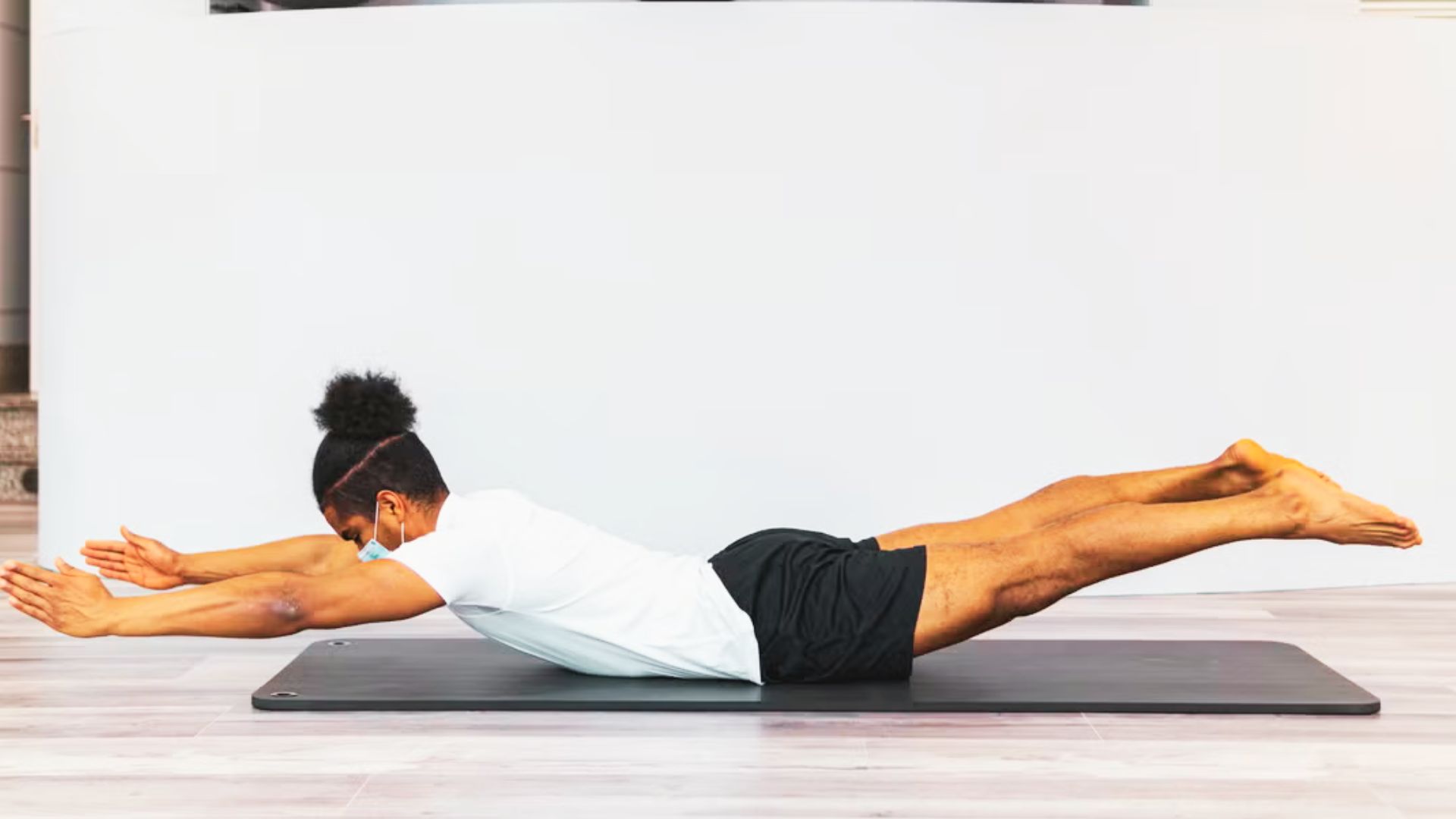Man on exercise mat lifting arms, chest, and legs off the floor in superman pose.