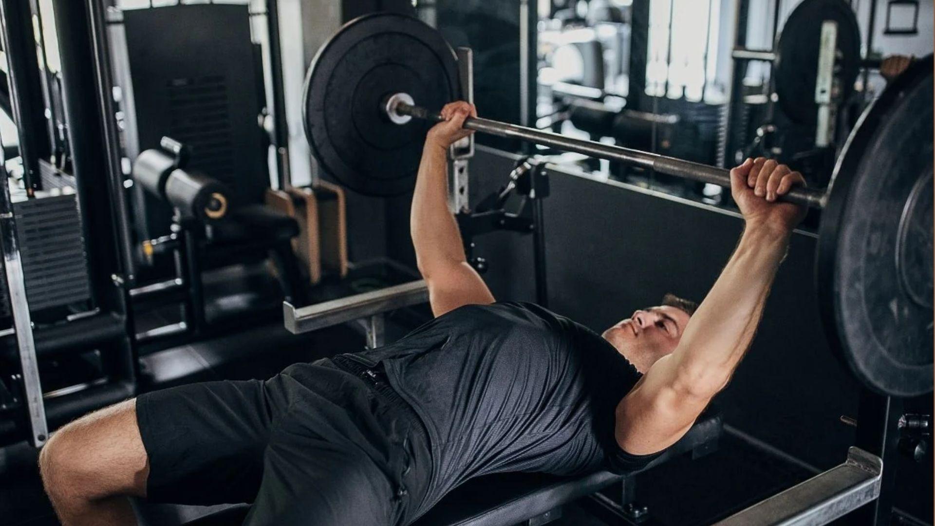A person performing a bench press in the gym, showing how strength levels vary based on lifting experience.