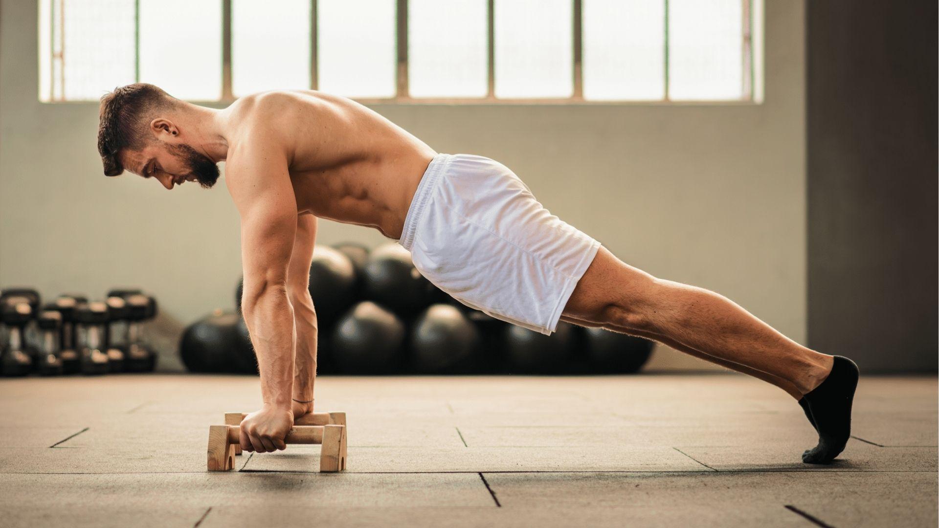 Man holds push-up position on parallettes in gym advancing to push variations for 30-day plan