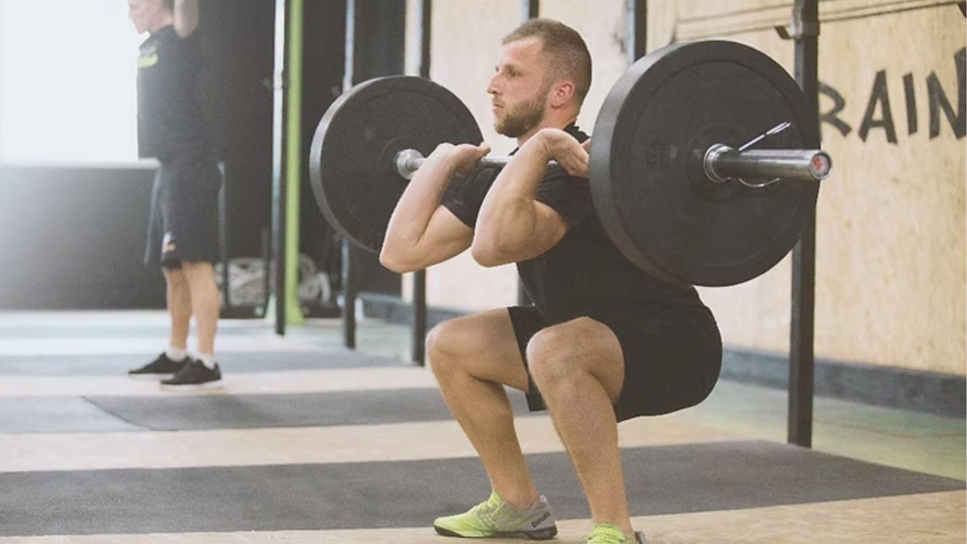 Athlete in bottom of a squat clean catching a loaded barbell on shoulders in a gym.