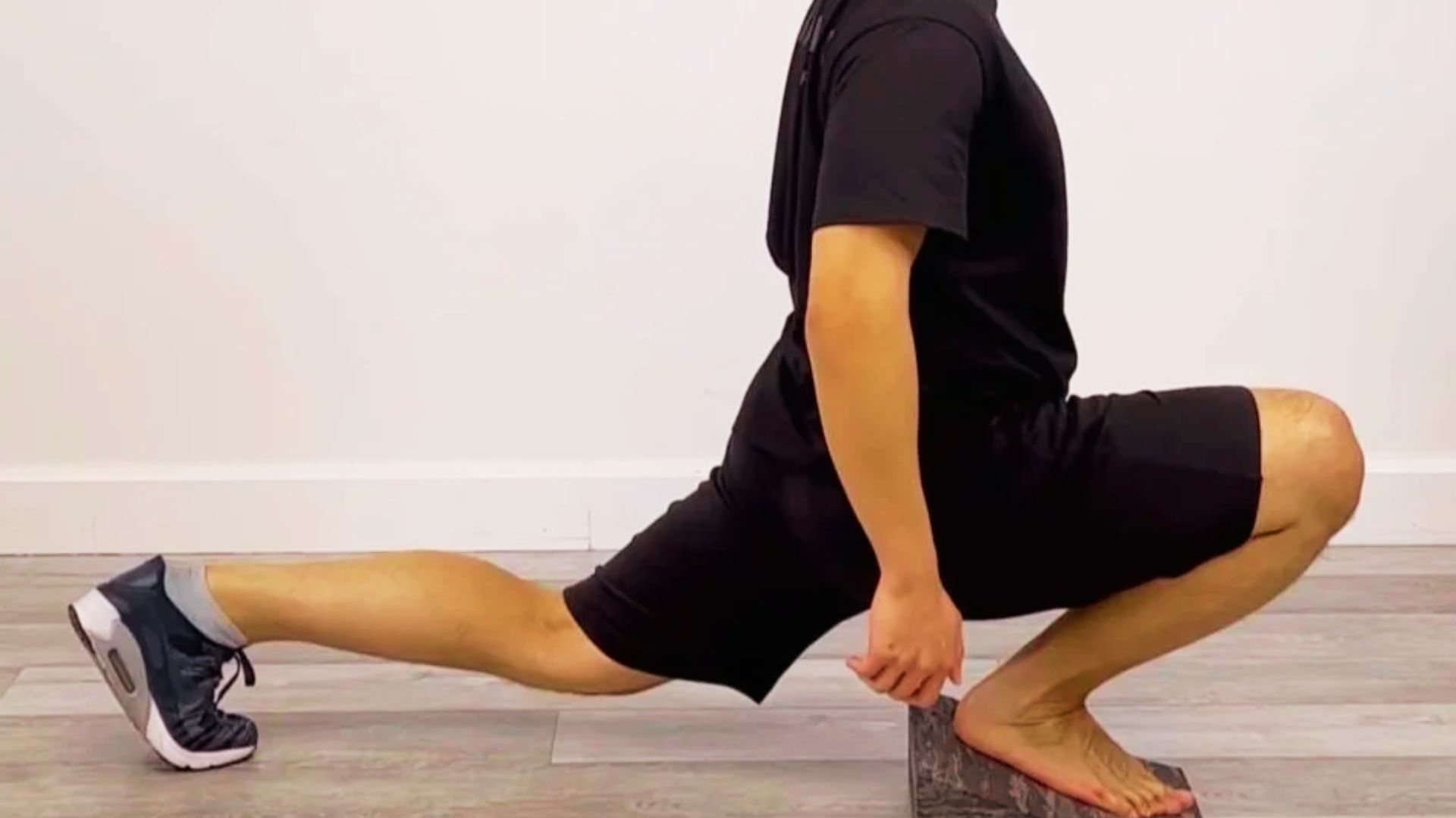 A man in a deep lunge position places his front foot flat on a slant board.