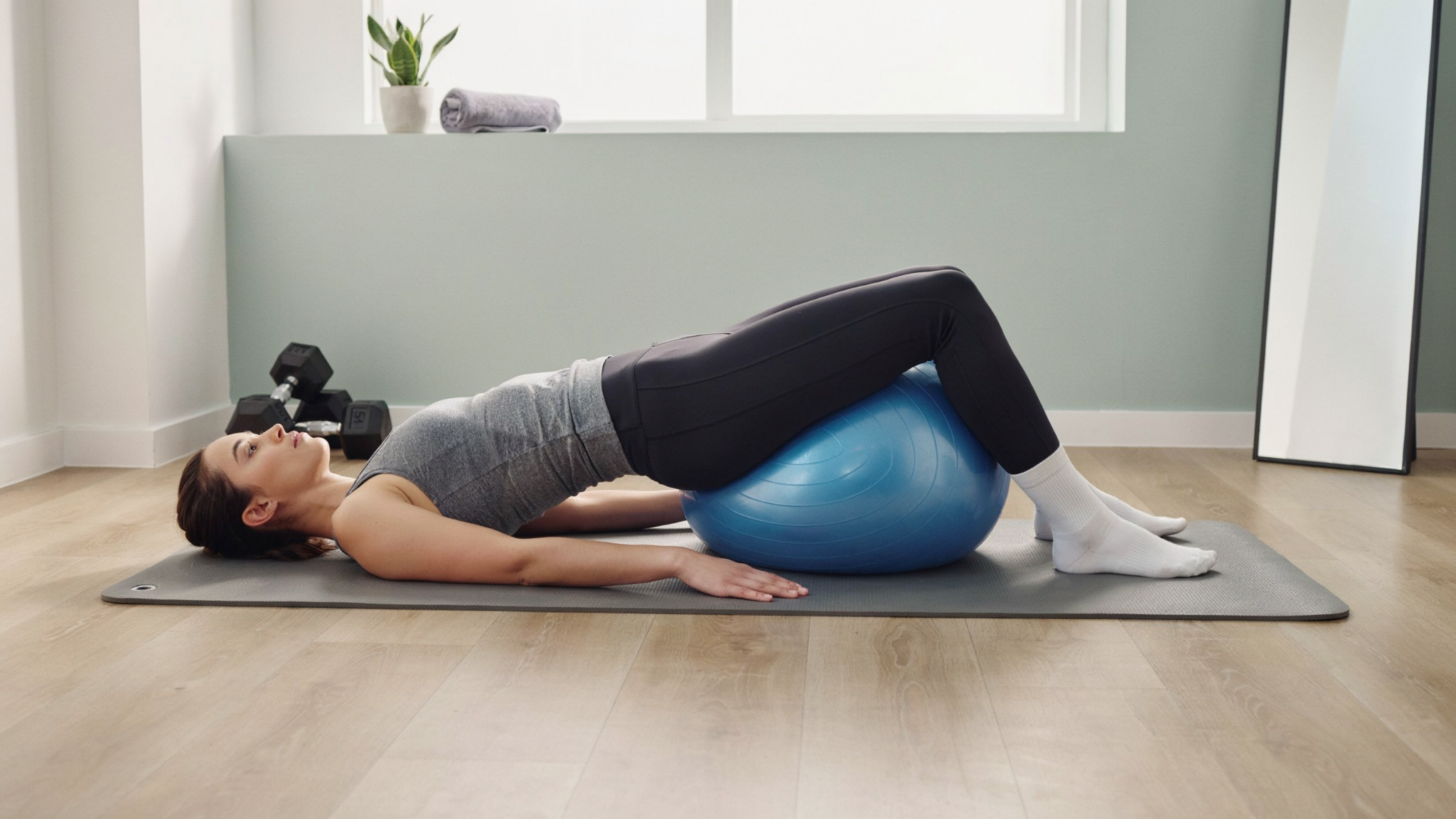Person lying on the floor with feet on a stability ball, lifting hips and curling the ball inward to strengthen hamstrings and core.