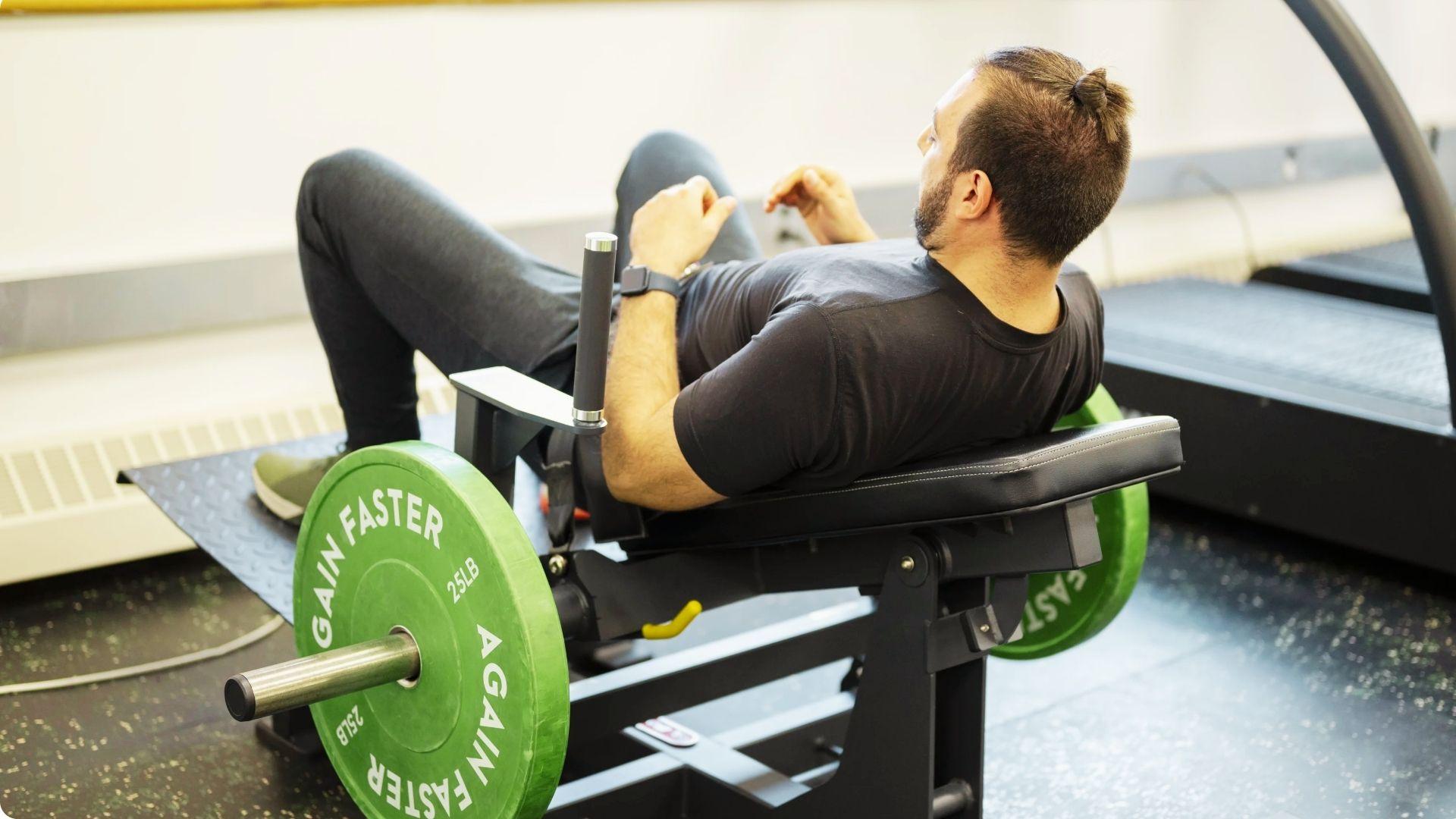 Person using a glute bridge machine, driving the hips upward to activate the glutes and hamstrings.