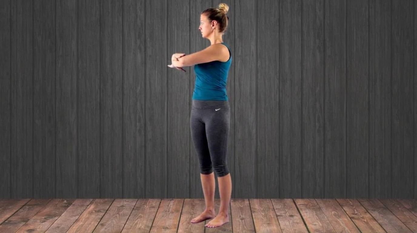Woman in a teal tank top stands barefoot with arms crossed in front of her chest, preparing to rotate.