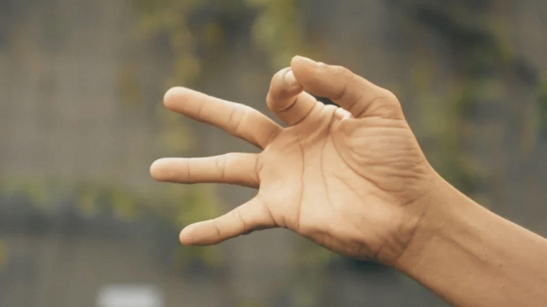 Close-up of left hand palm up with thumb folded across palm, fingers together, demonstrating thumb opposition stretch, plain