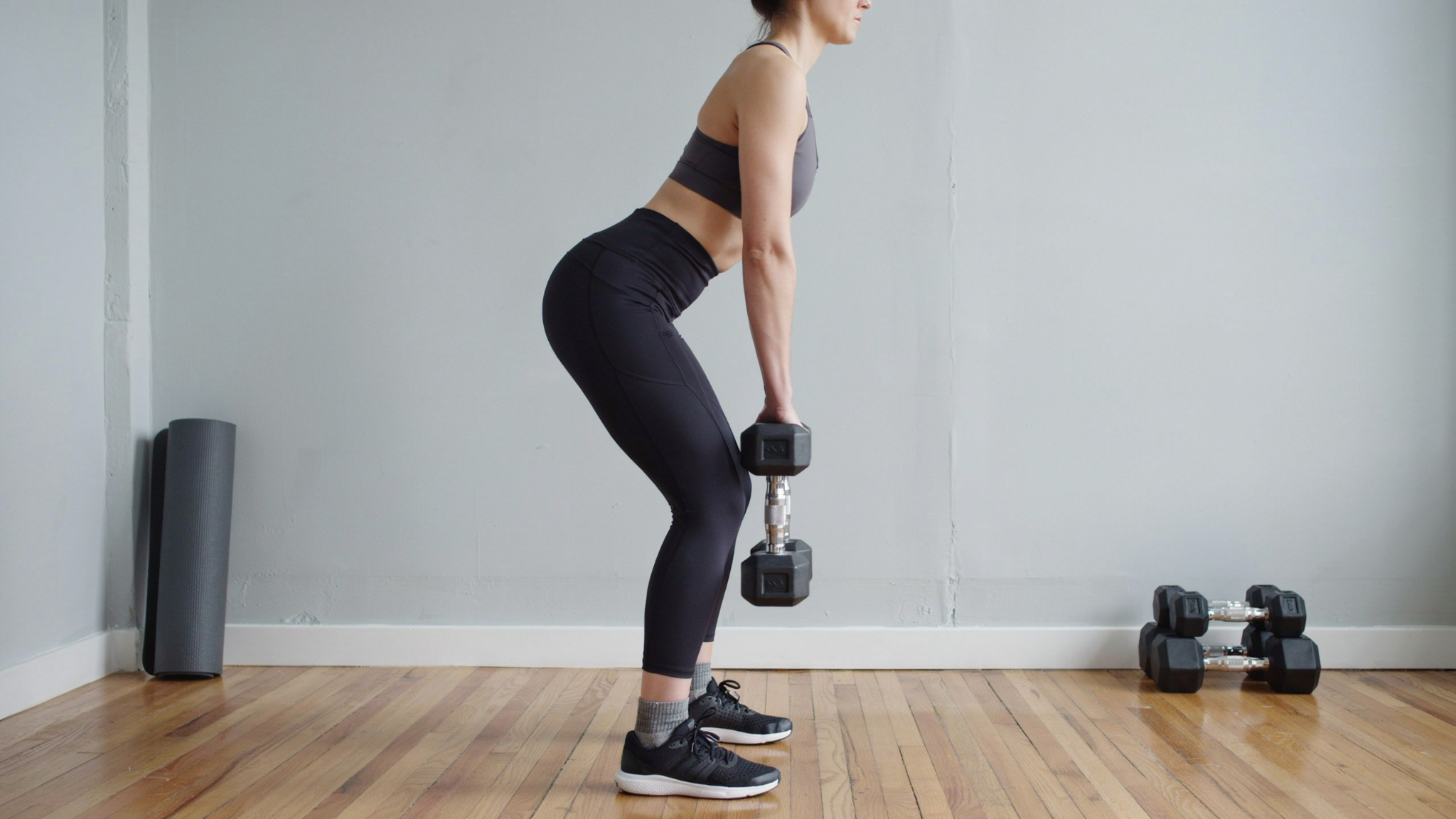 Person performing Romanian deadlift holding dumbbells, hinging at the hips with a flat back while lowering weights to stretch and strengthen hamstrings.