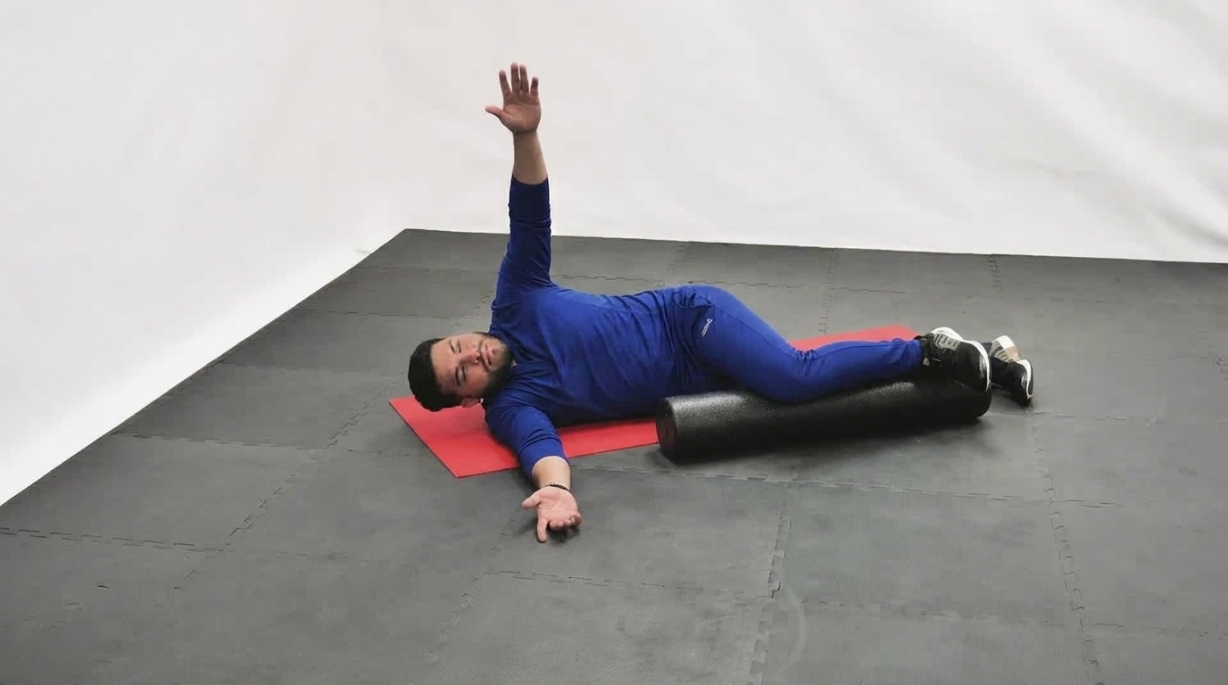 Man in blue activewear lies on his side on a foam roller with one arm raised and the other extended.