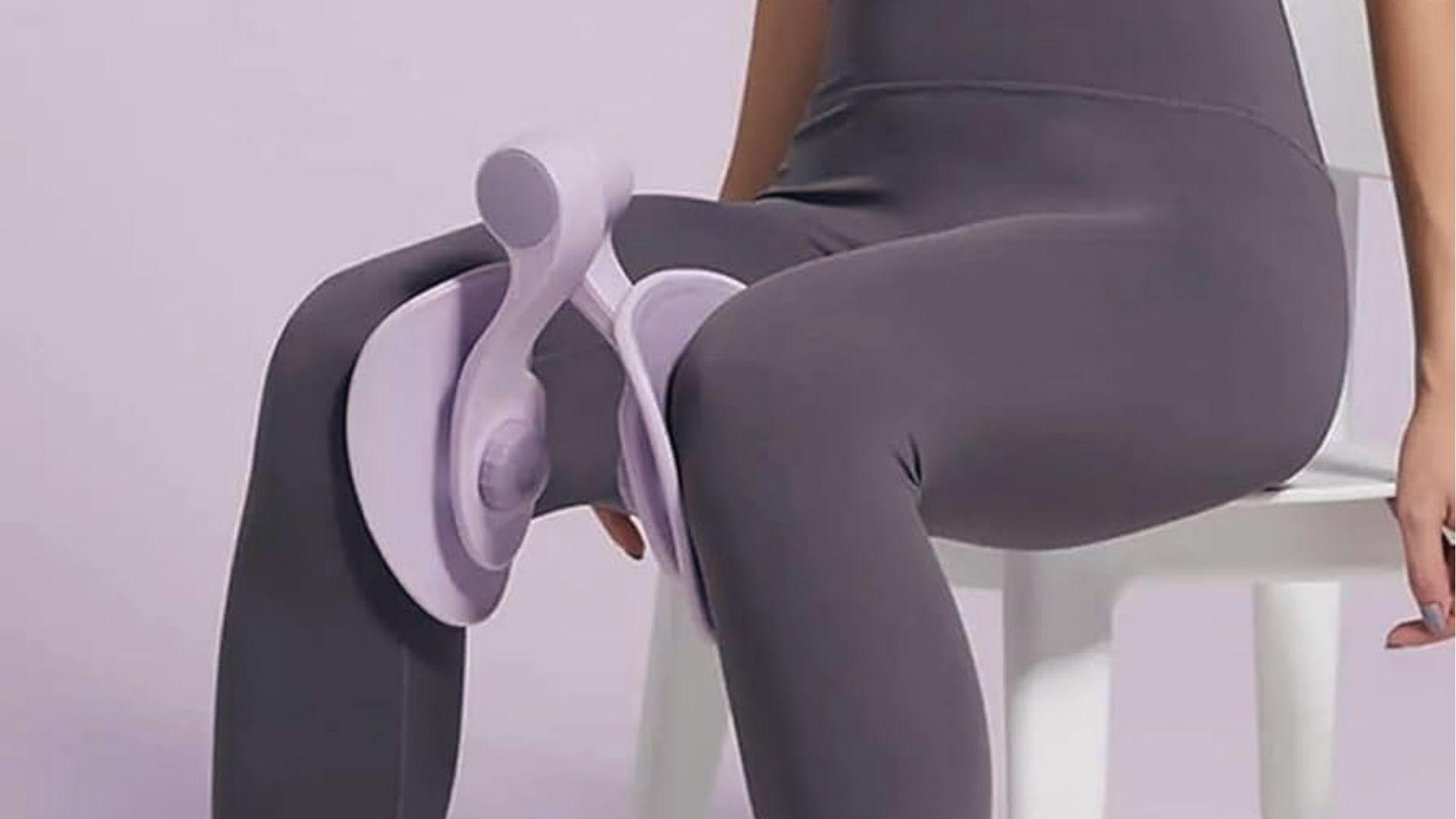 Woman in gray leggings seated on white chair squeezing lavender Thigh Master between inner thighs.