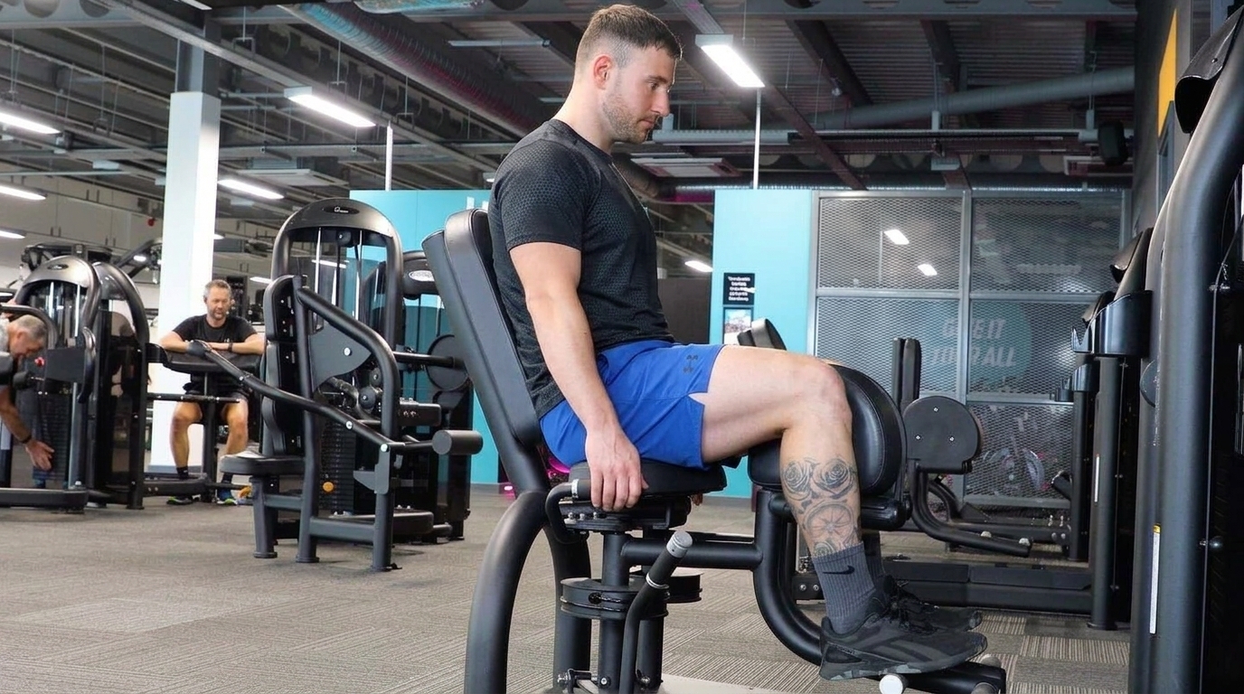 Man in black shirt and blue shorts seated on a hip abduction machine with pads against his outer thighs.