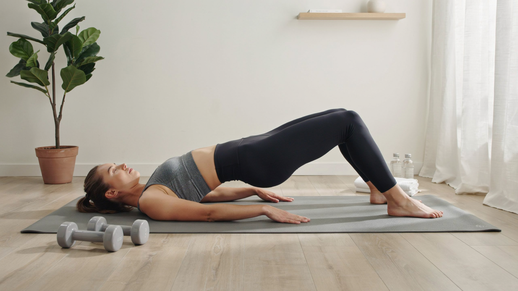 Person lying on a yoga mat performing a glute bridge, lifting hips upward while keeping knees bent and feet flat on the floor to activate glutes and hamstrings.