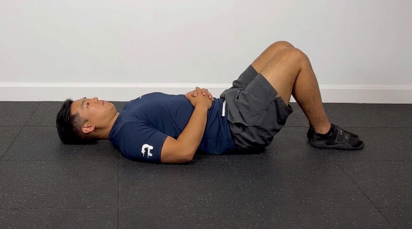 Man performing chin tuck exercise lying flat on gym floor with knees bent and hands on stomach