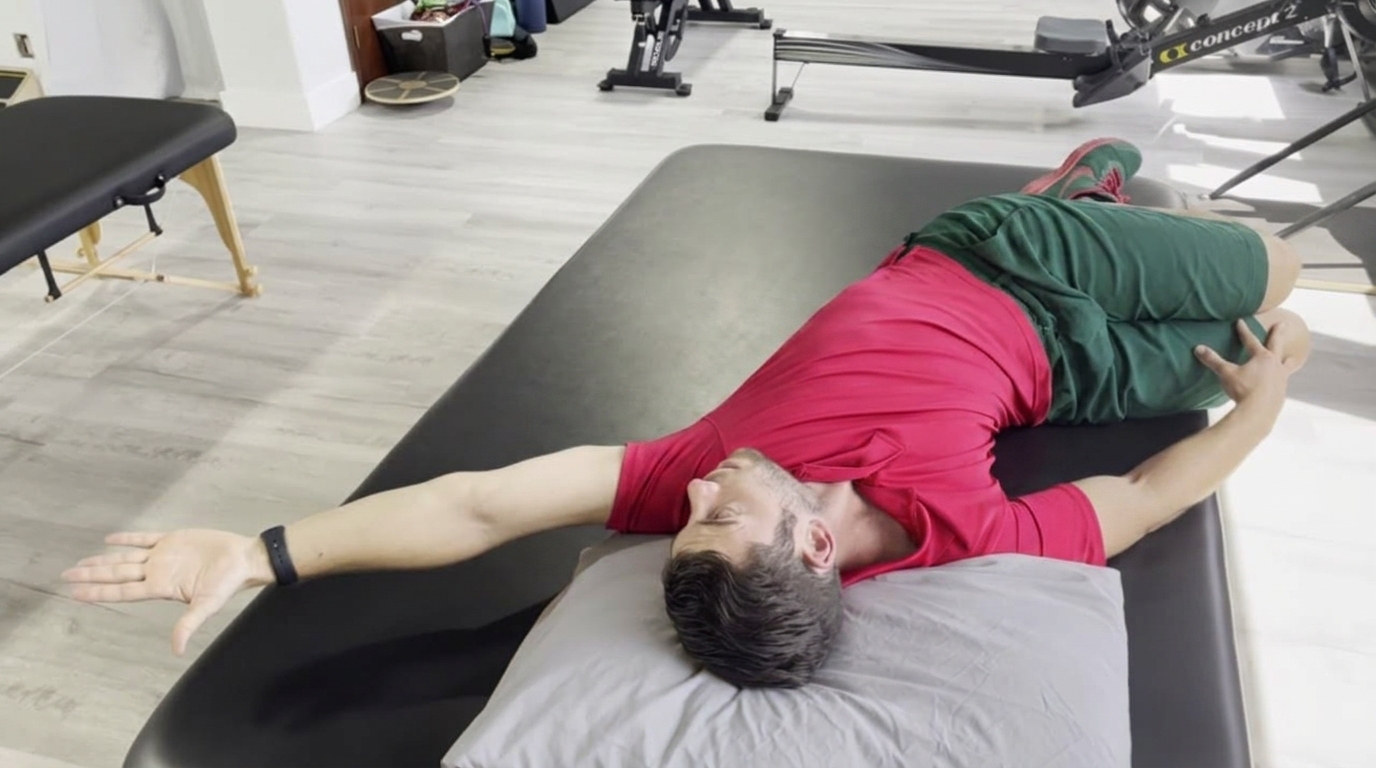 Man in a red shirt lies on a treatment table with knees bent to one side and arms outstretched.