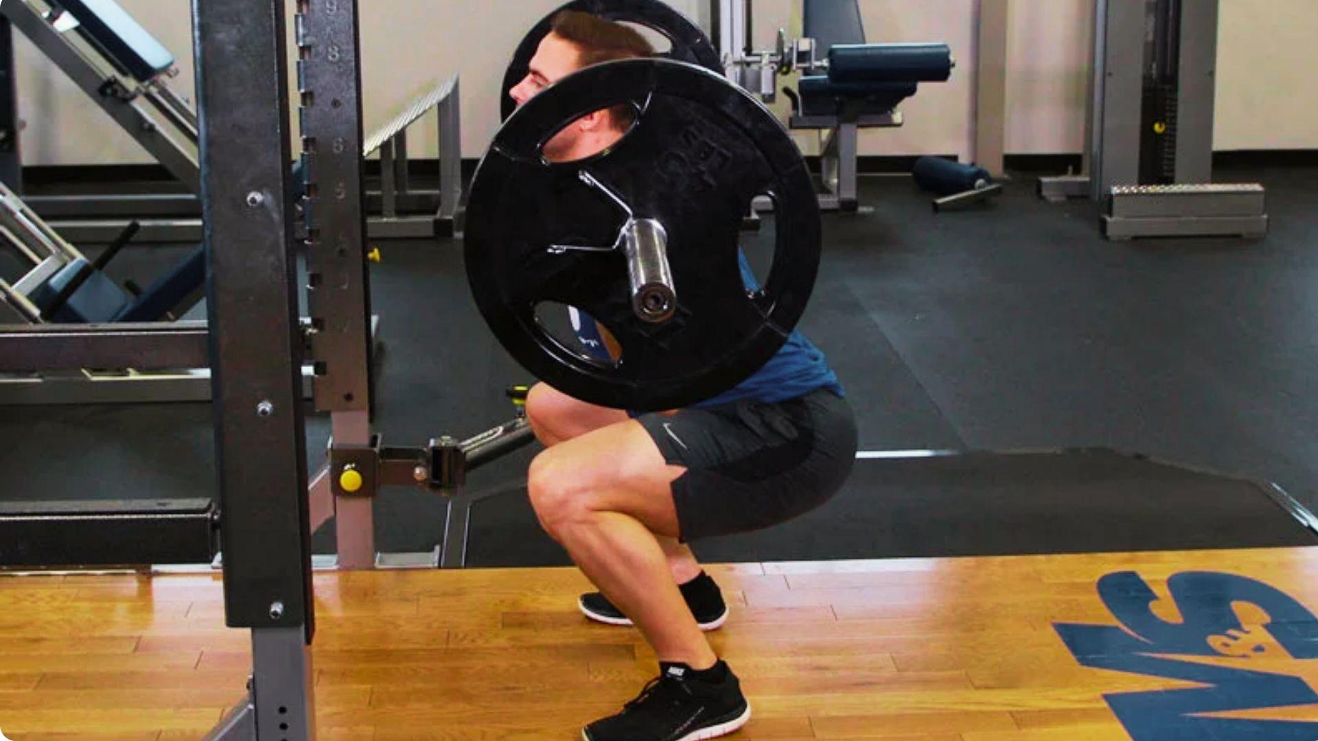 Athlete performing a barbell back squat with the bar resting across the upper back while lowering into a deep squat position.