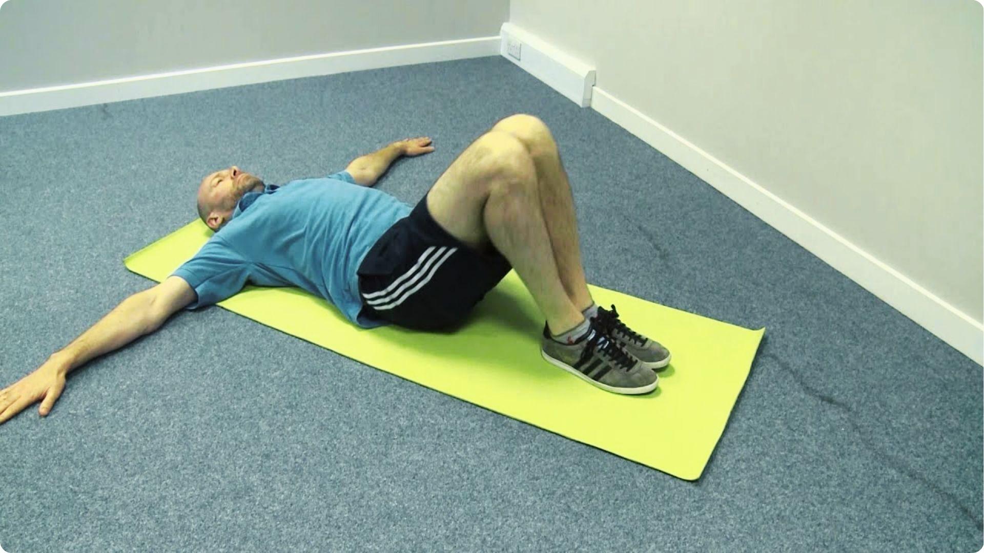 Man in a blue polo lies on a yellow mat with knees bent and arms extended in a T position.