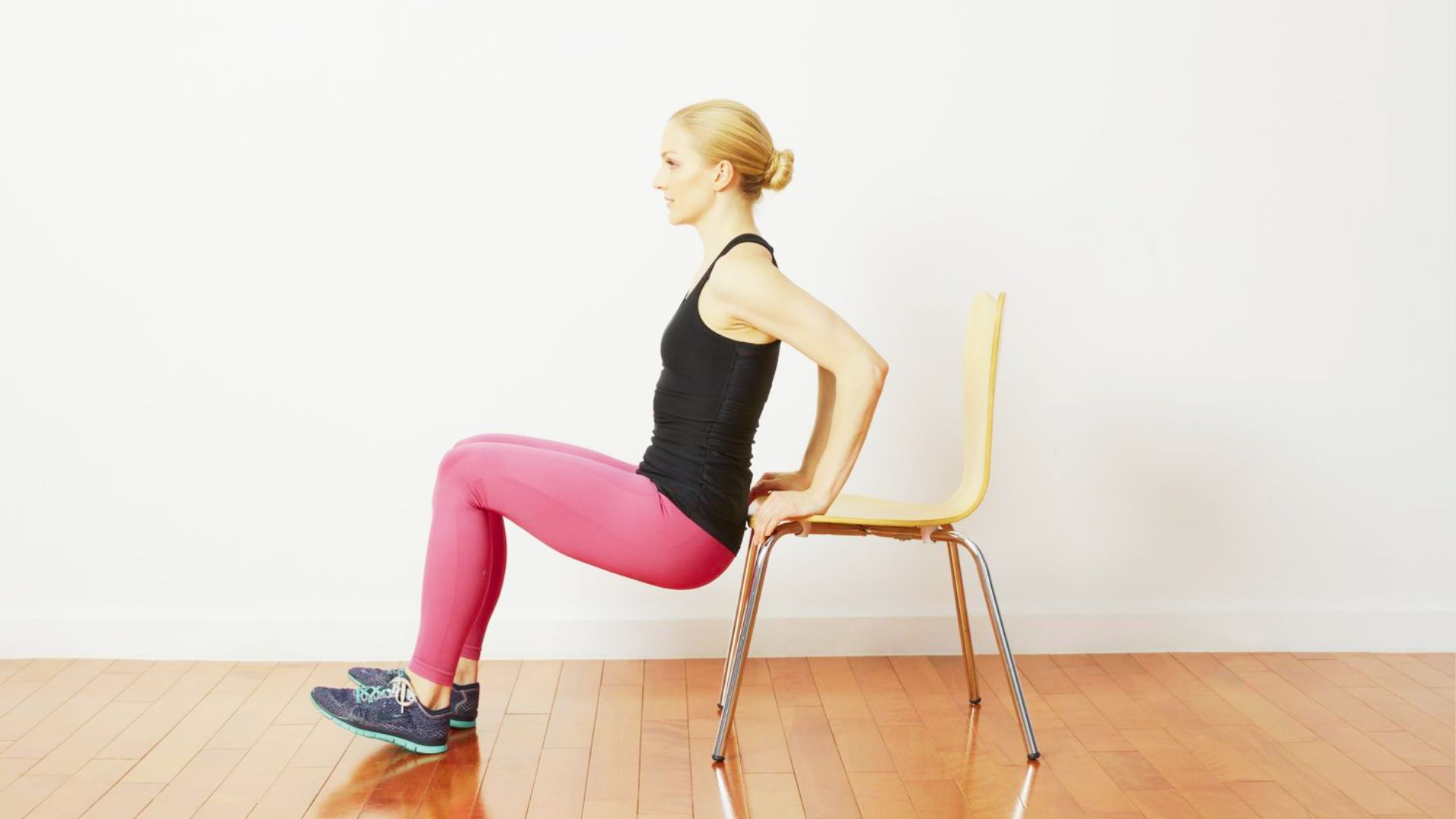 A woman in athletic wear performing a triceps bench dip using a stable wooden chair.