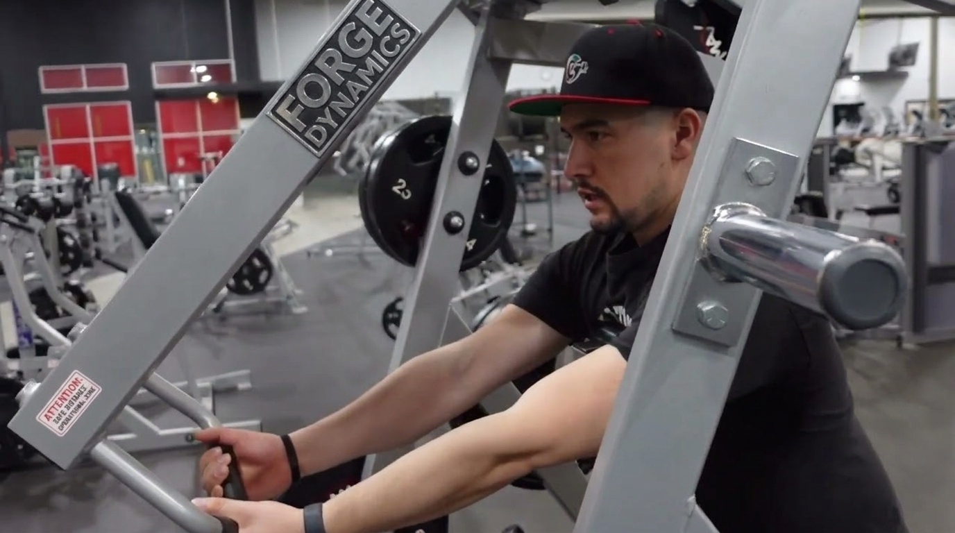 Man in a black cap seated at a Forge Dynamics Iso Lateral Row machine, gripping both handles at full extension.