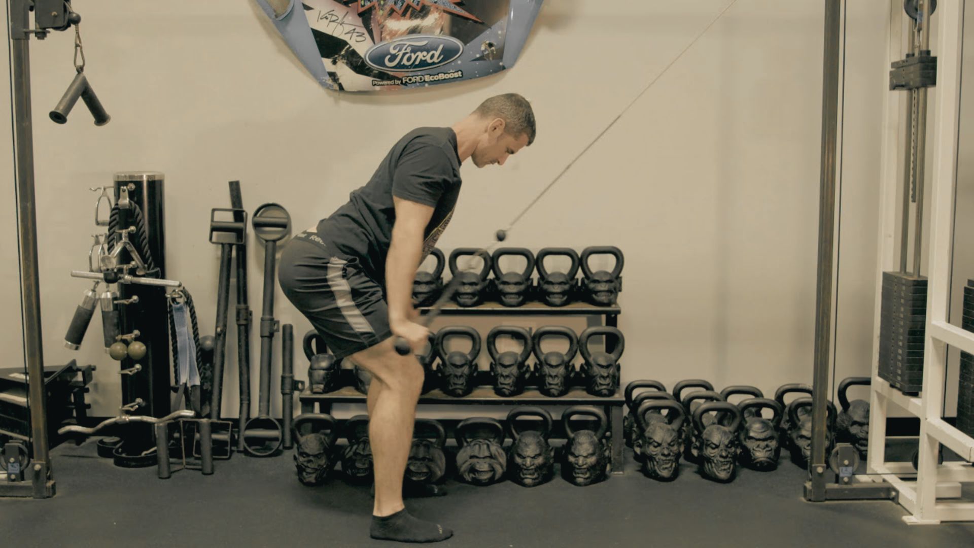 Man in black shirt and shorts performing a bent-over cable row with a straight bar attachment.