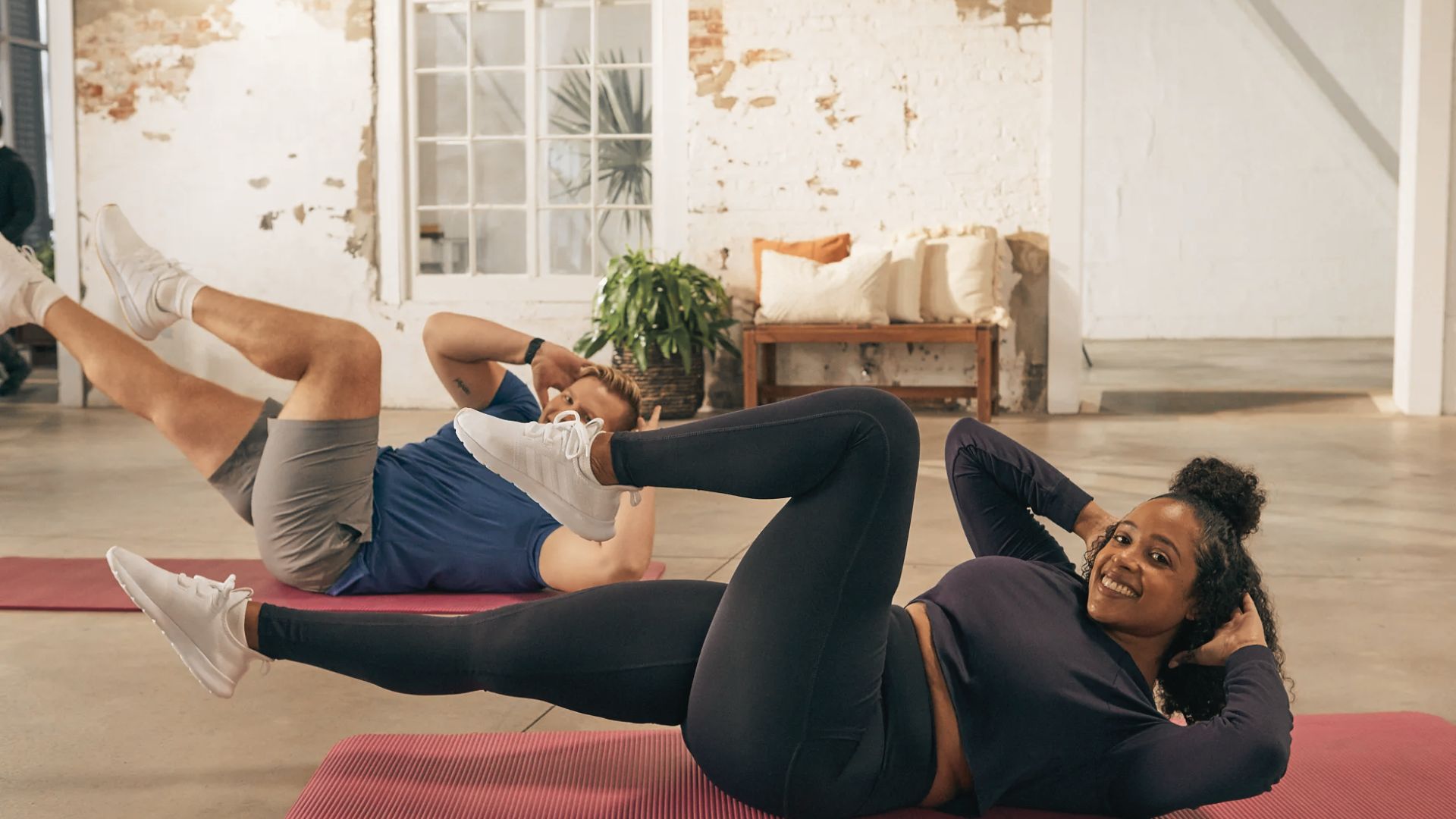 Woman holding a Pilates plank with one leg lifted, engaging her core on a mat in a bright studio.