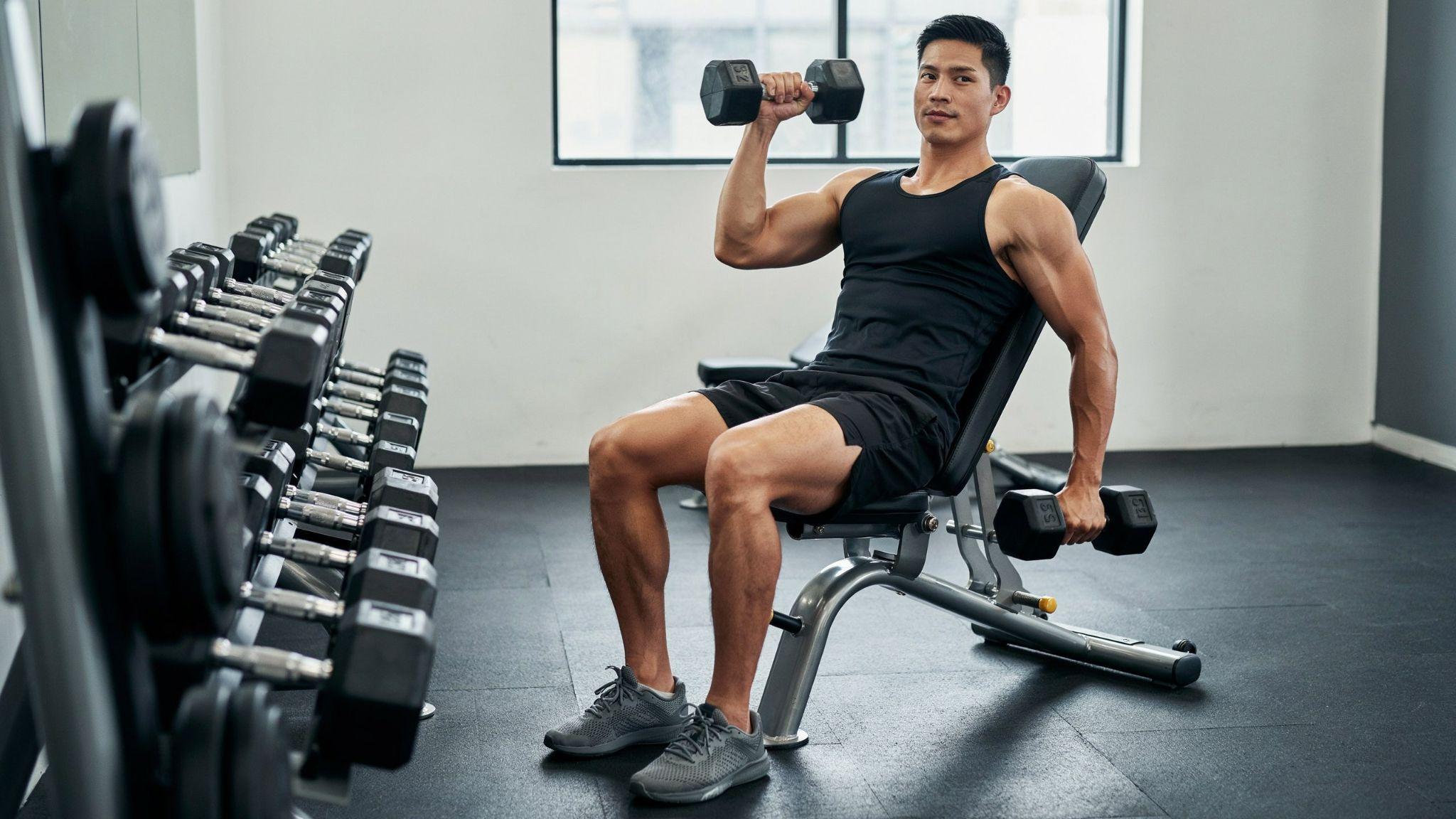 A man performing an incline dumbbell curl on an incline bench inside a gym.